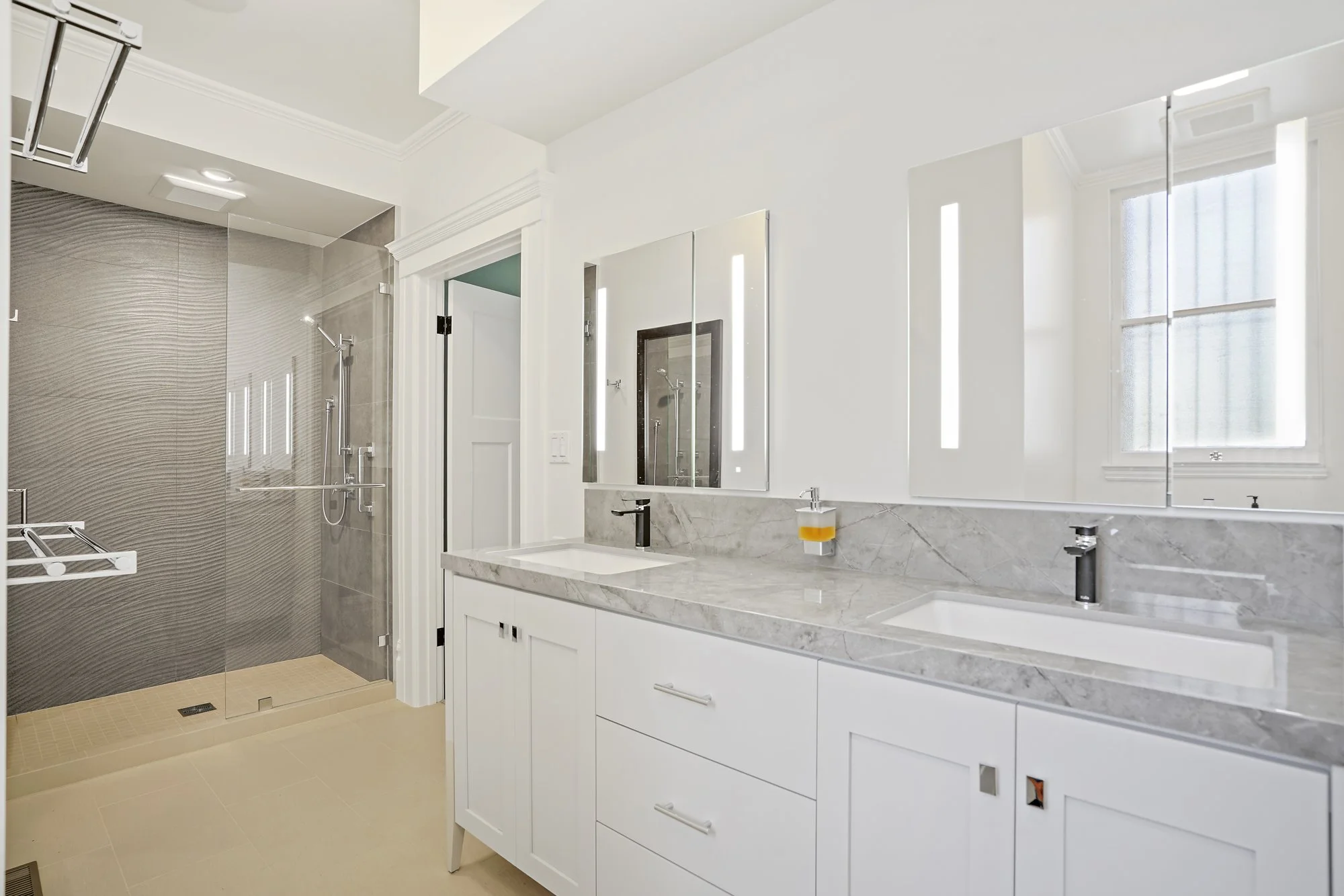 Double-vanity bathroom with white cabinets, a marble countertop, dual mirrors, and a textured-tile walk-in shower
