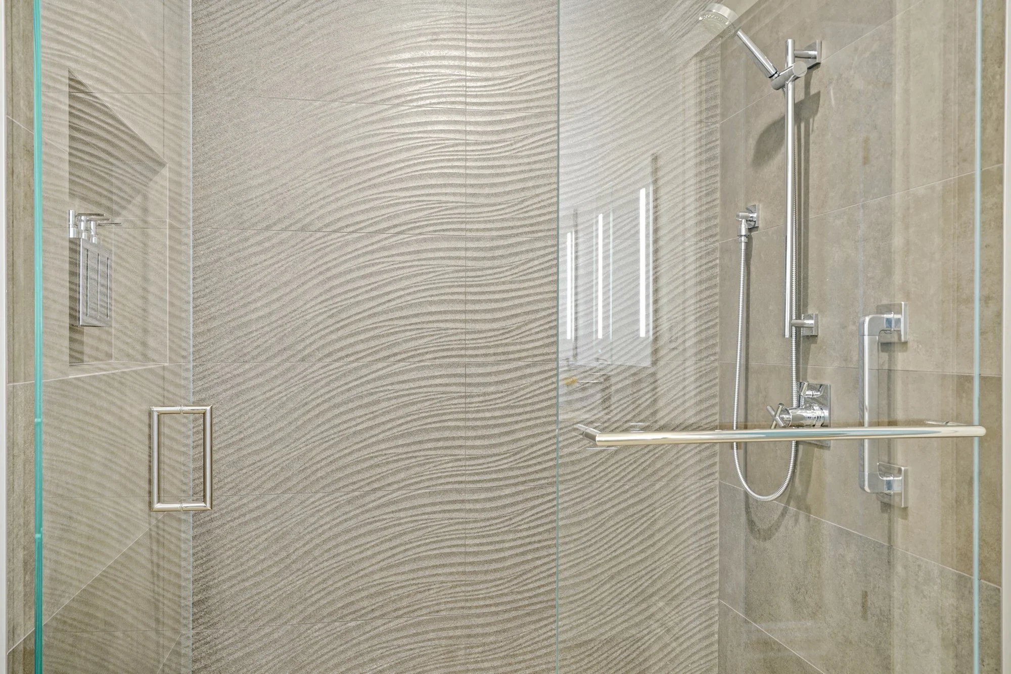 Walk-in shower with wavy textured stone-look tile walls, a glass enclosure, and both a fixed and handheld showerhead