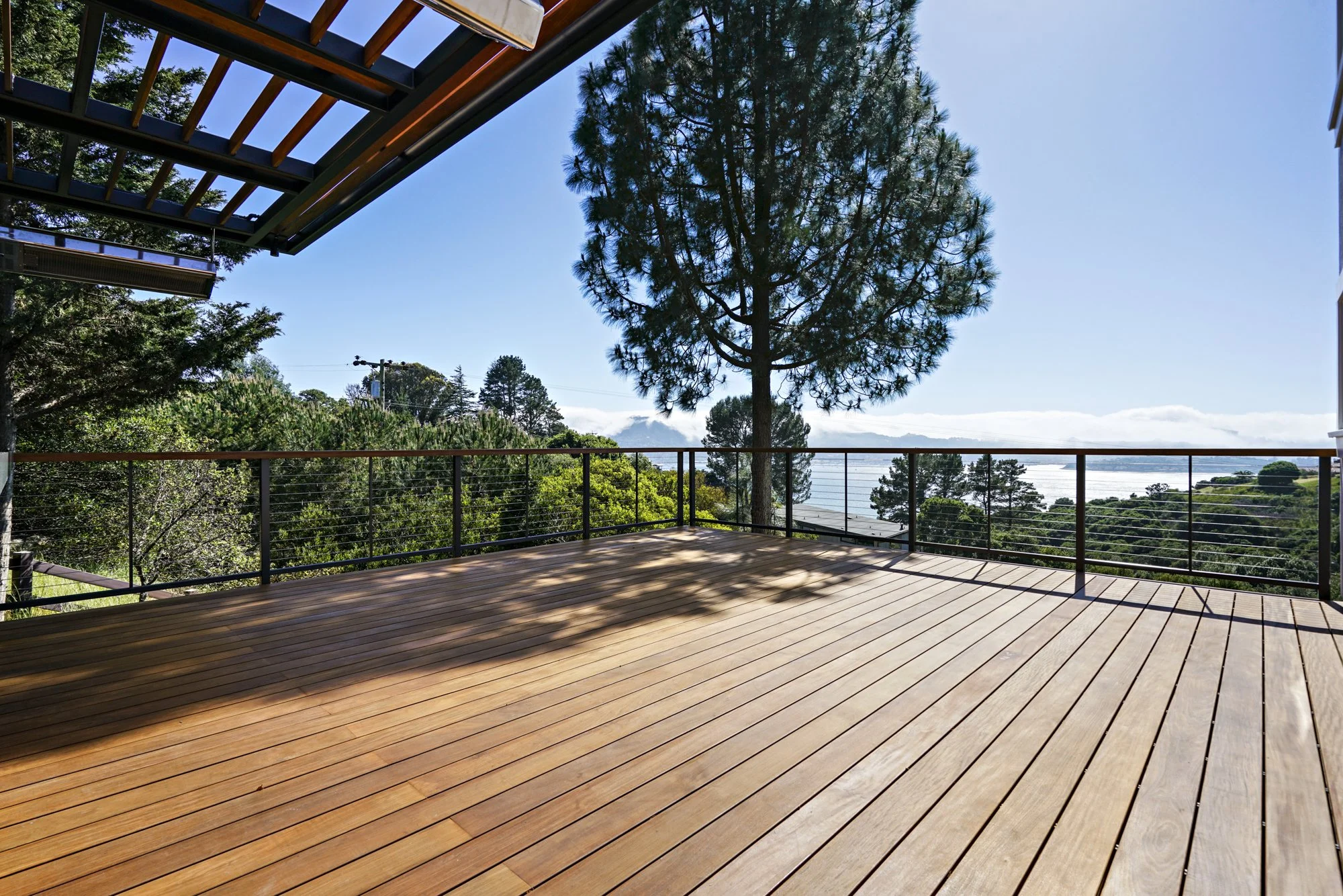 Wood deck with a cable railing and a wood pergola, framed by mature trees and a panoramic bay view