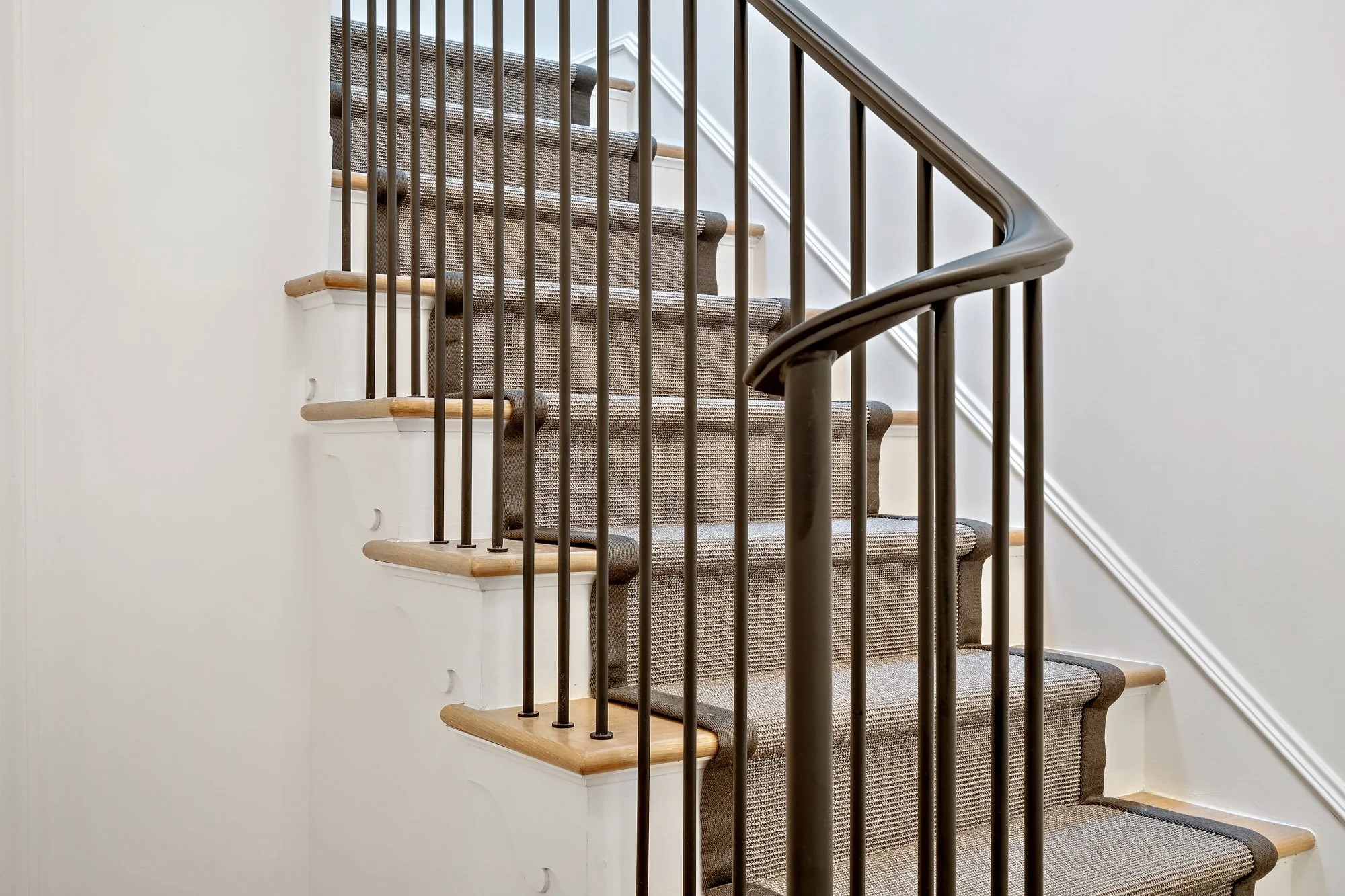 Staircase with wood treads, a woven runner, black metal balusters, and white walls