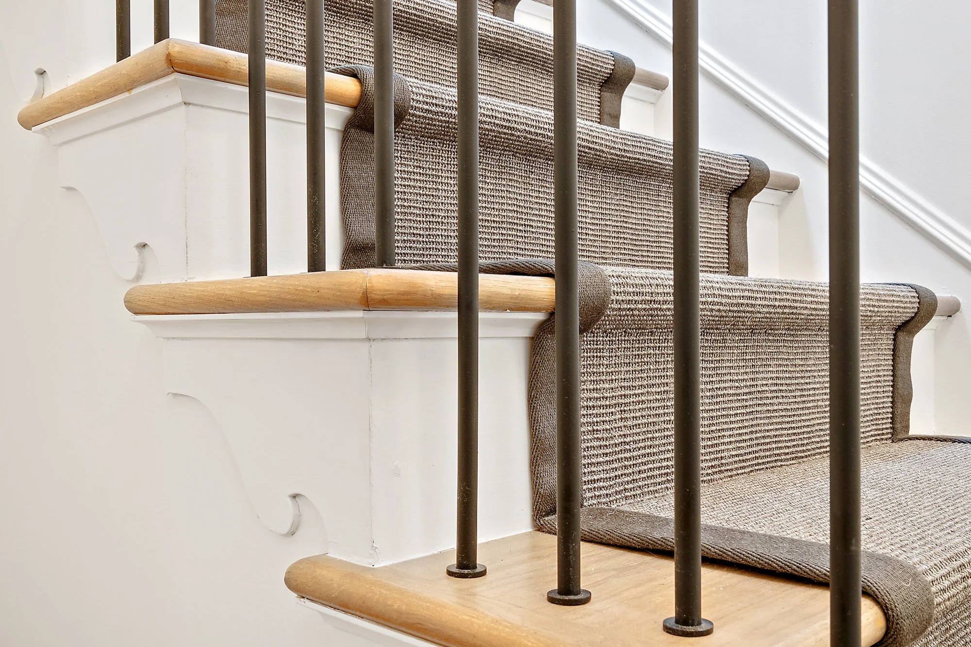 Detail of a curved staircase with a woven runner, wood treads, and a black metal railing