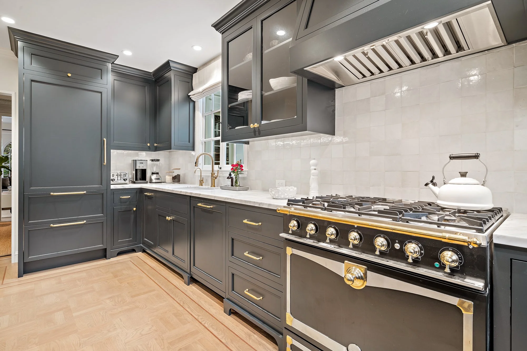 Gray shaker kitchen with a black-and-brass professional range, marble backsplash, and brass cabinet pulls