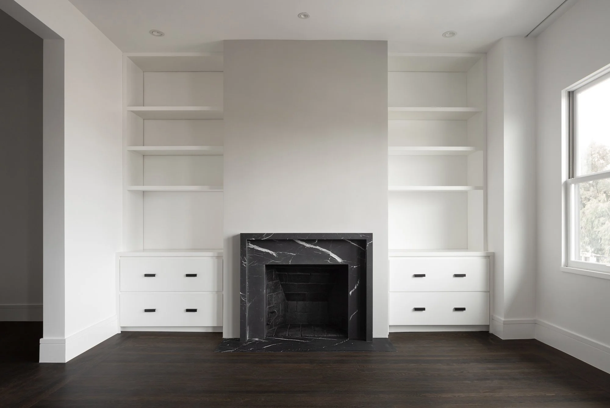 White living room with a black marble fireplace, built-in shelving, base drawers, and dark hardwood floors