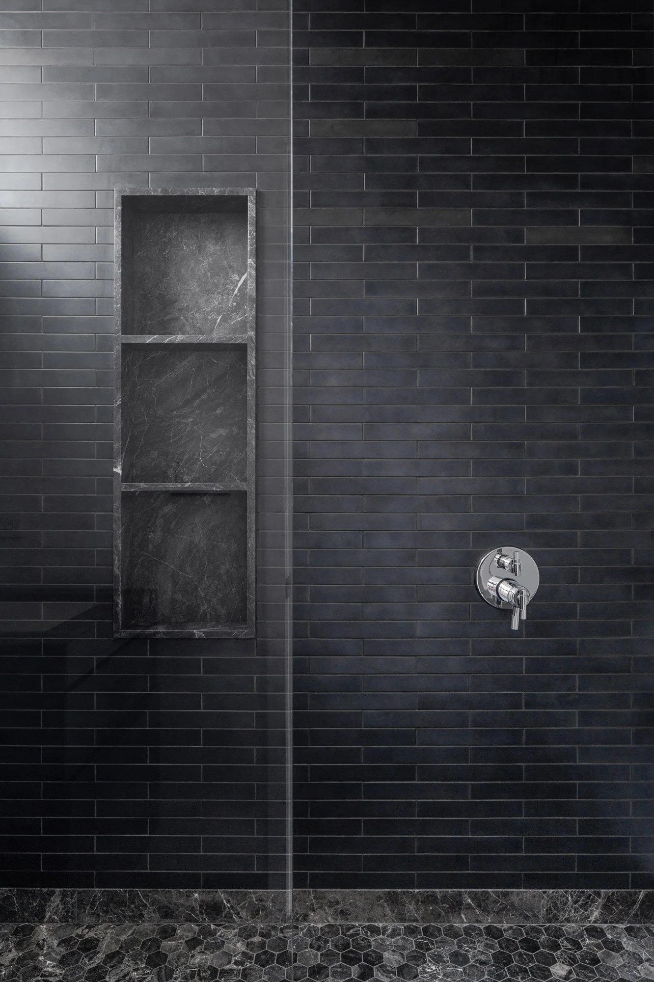 Walk-in shower with black stacked-tile walls, a recessed niche, and a stone mosaic floor