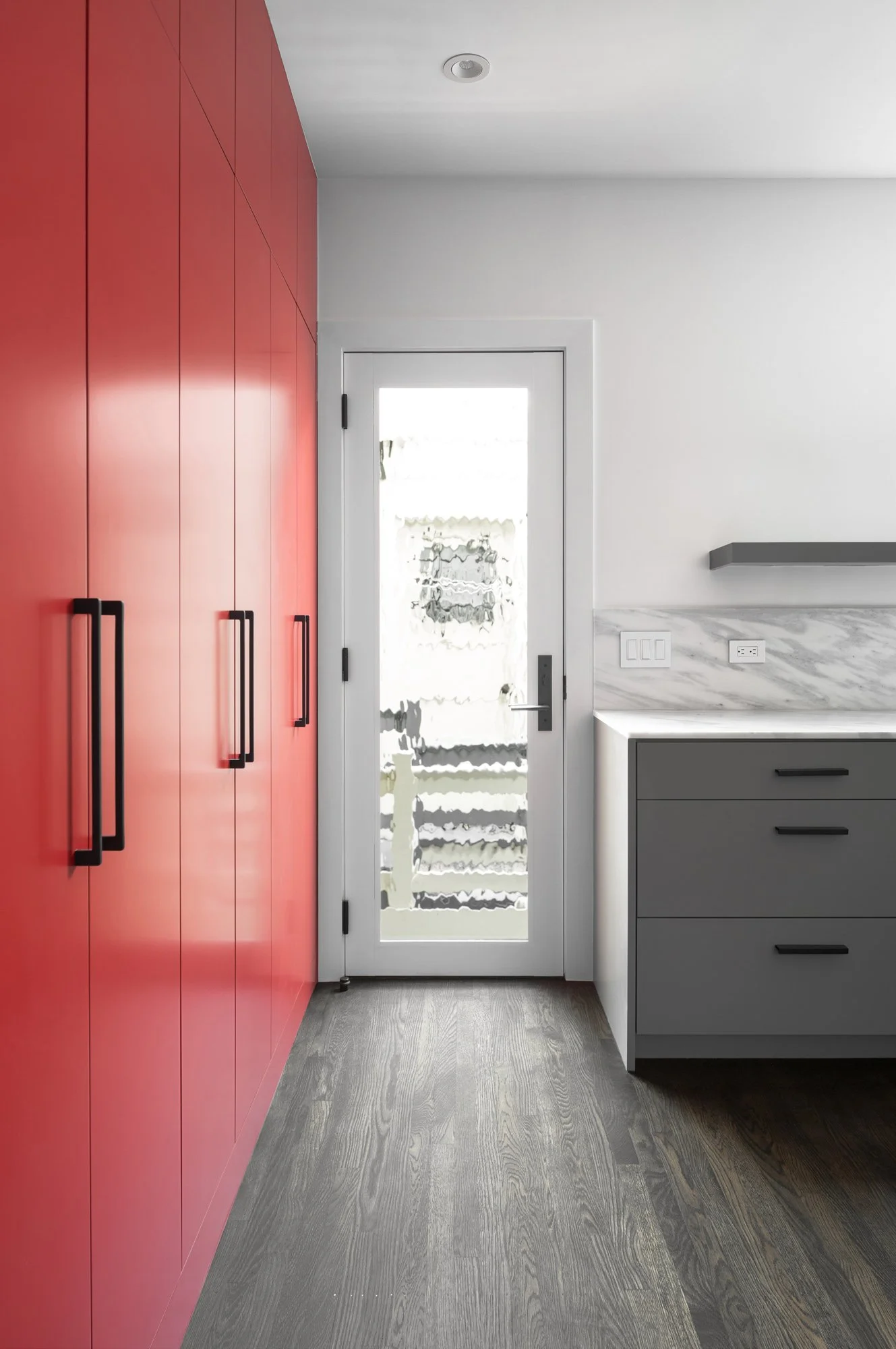 Narrow kitchen view with tall red cabinetry, black hardware, marble counters, and a glass door to the exterior