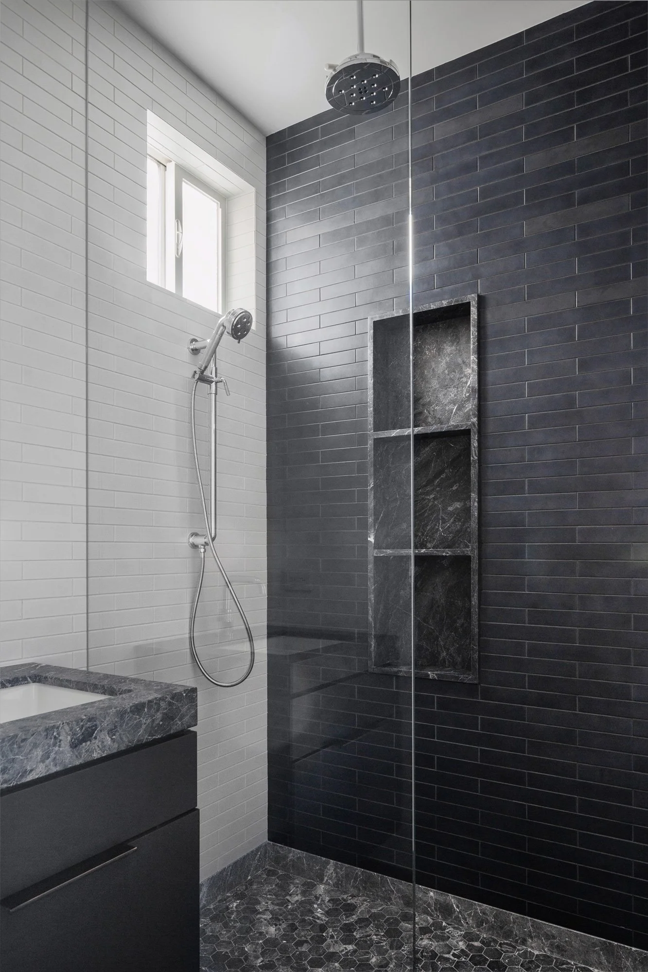Black-tiled walk-in shower with a rainfall showerhead, glass enclosure, and a stone floor