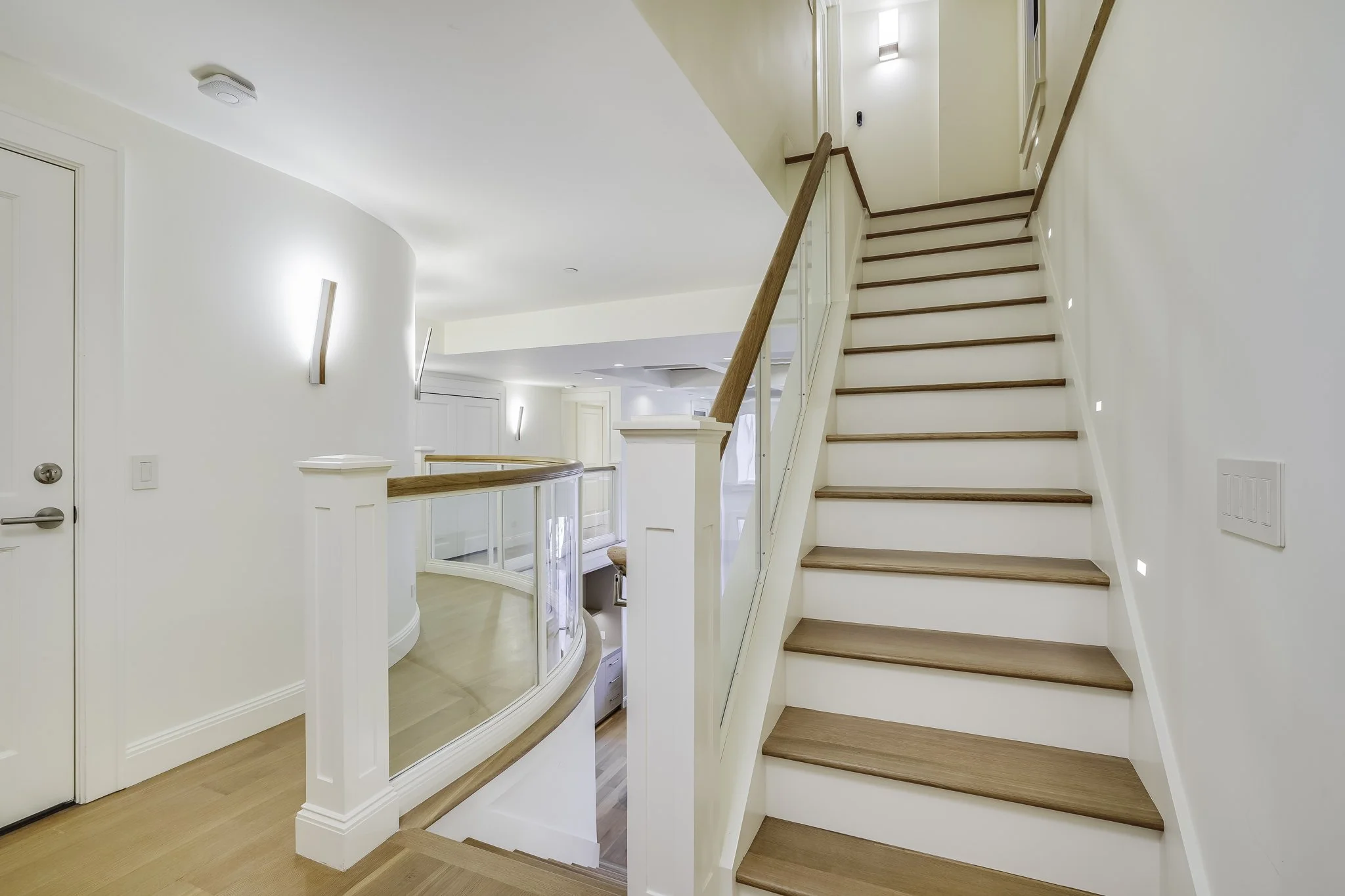 Light-filled landing with a curved wood-railed staircase, white walls, and pale hardwood floors