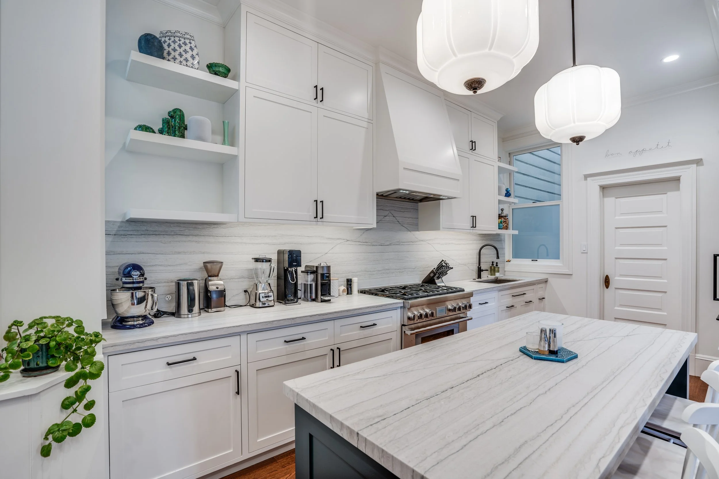 White kitchen with a marble-look waterfall island, open shelving, stainless range with hood, and white subway-tile backsplash