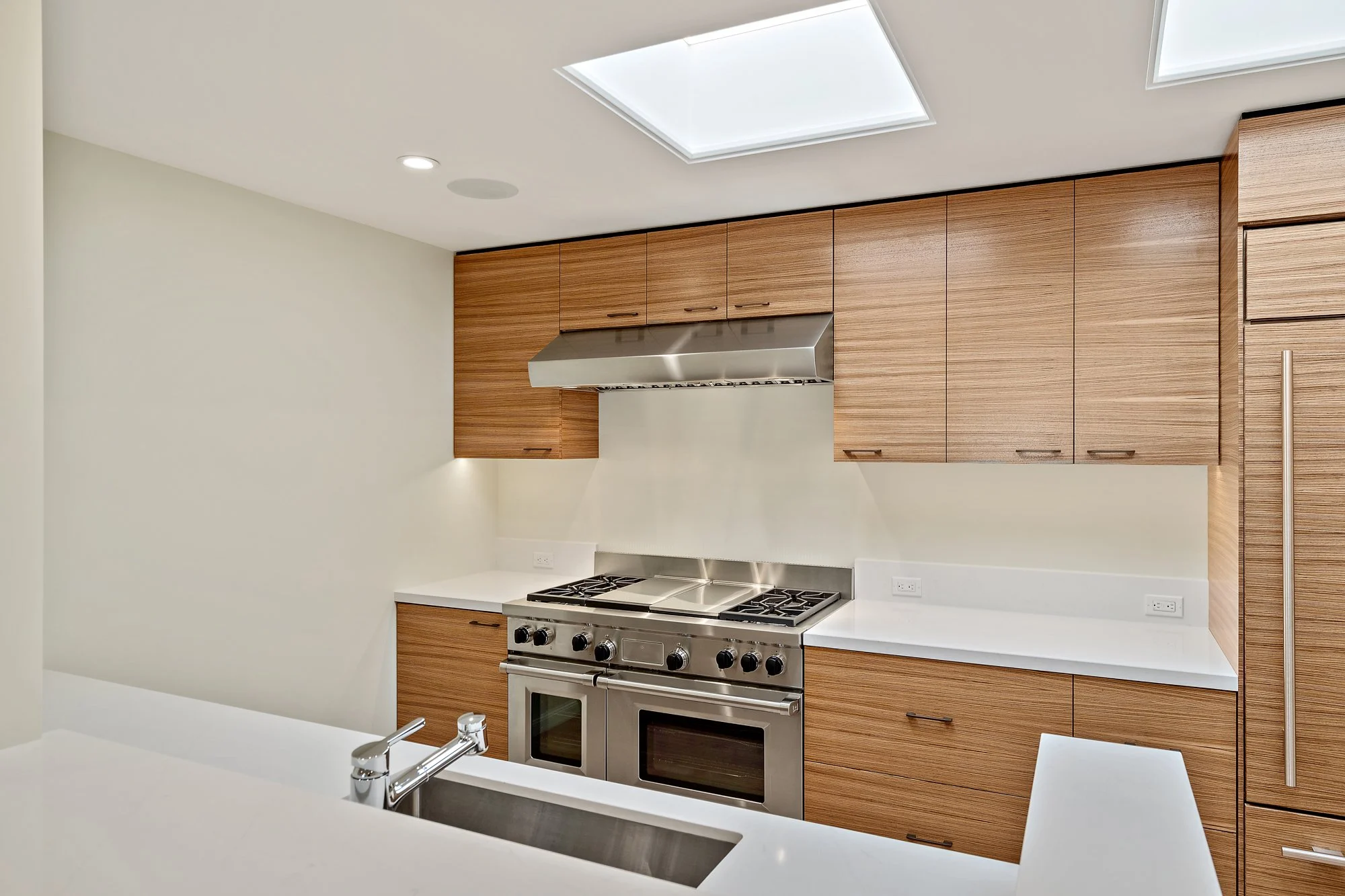 Kitchen with wood-grain cabinets, stainless range and hood, a waterfall-edge island with an integrated sink, and skylights