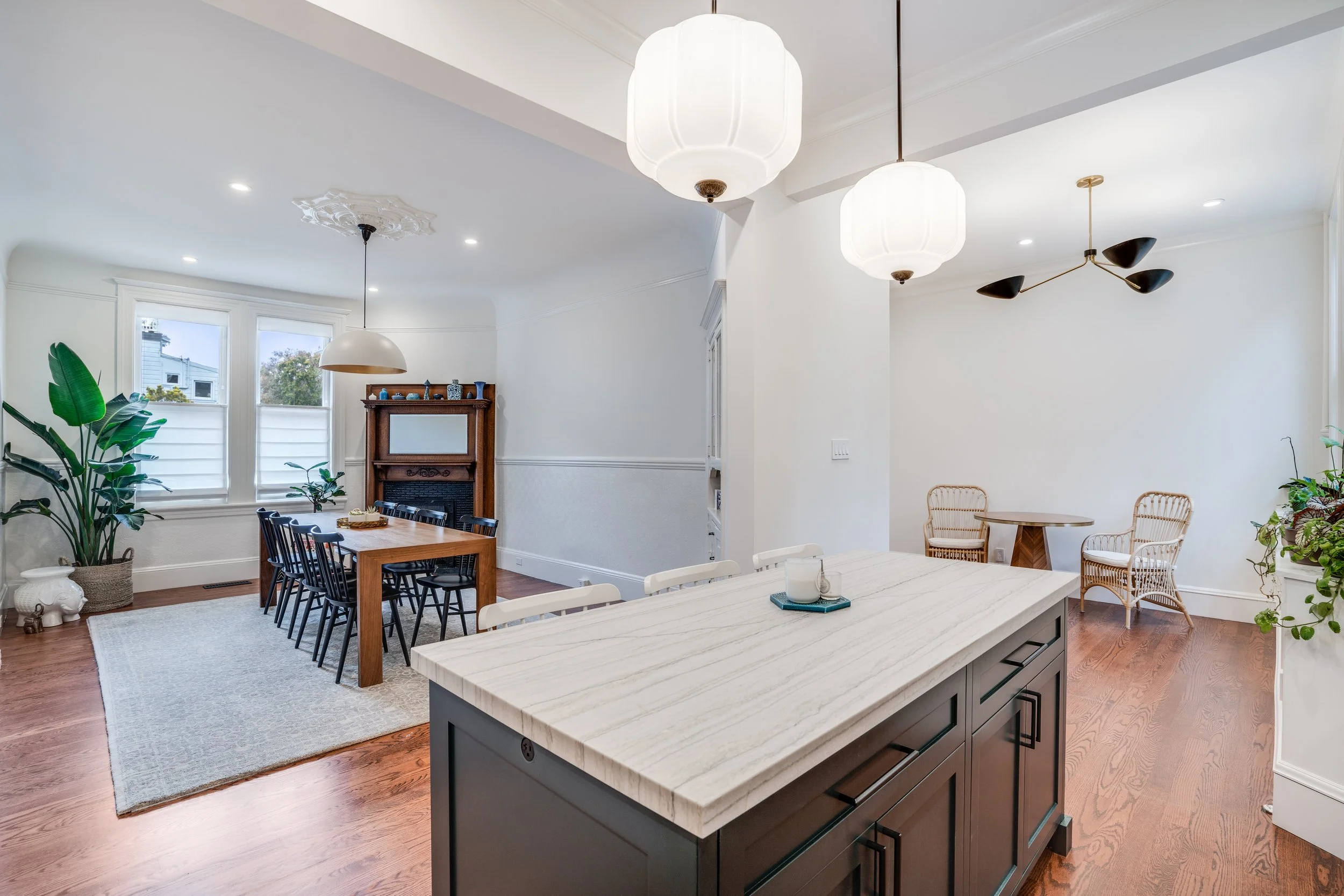Open-plan living and dining room with a marble-look island, globe pendants, hardwood floors, and a fireplace seating area