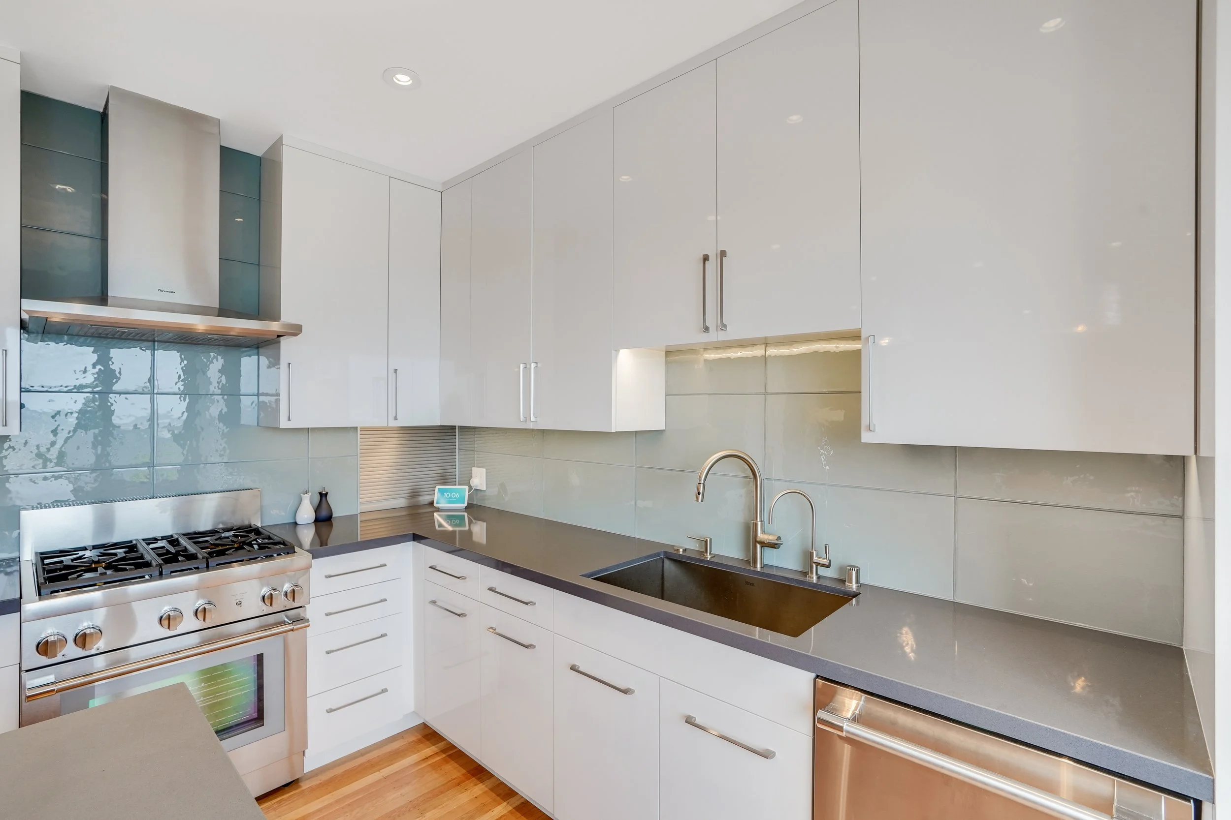 White kitchen with a stainless gas range, glass-tile backsplash, stainless countertop, and undermount sink
