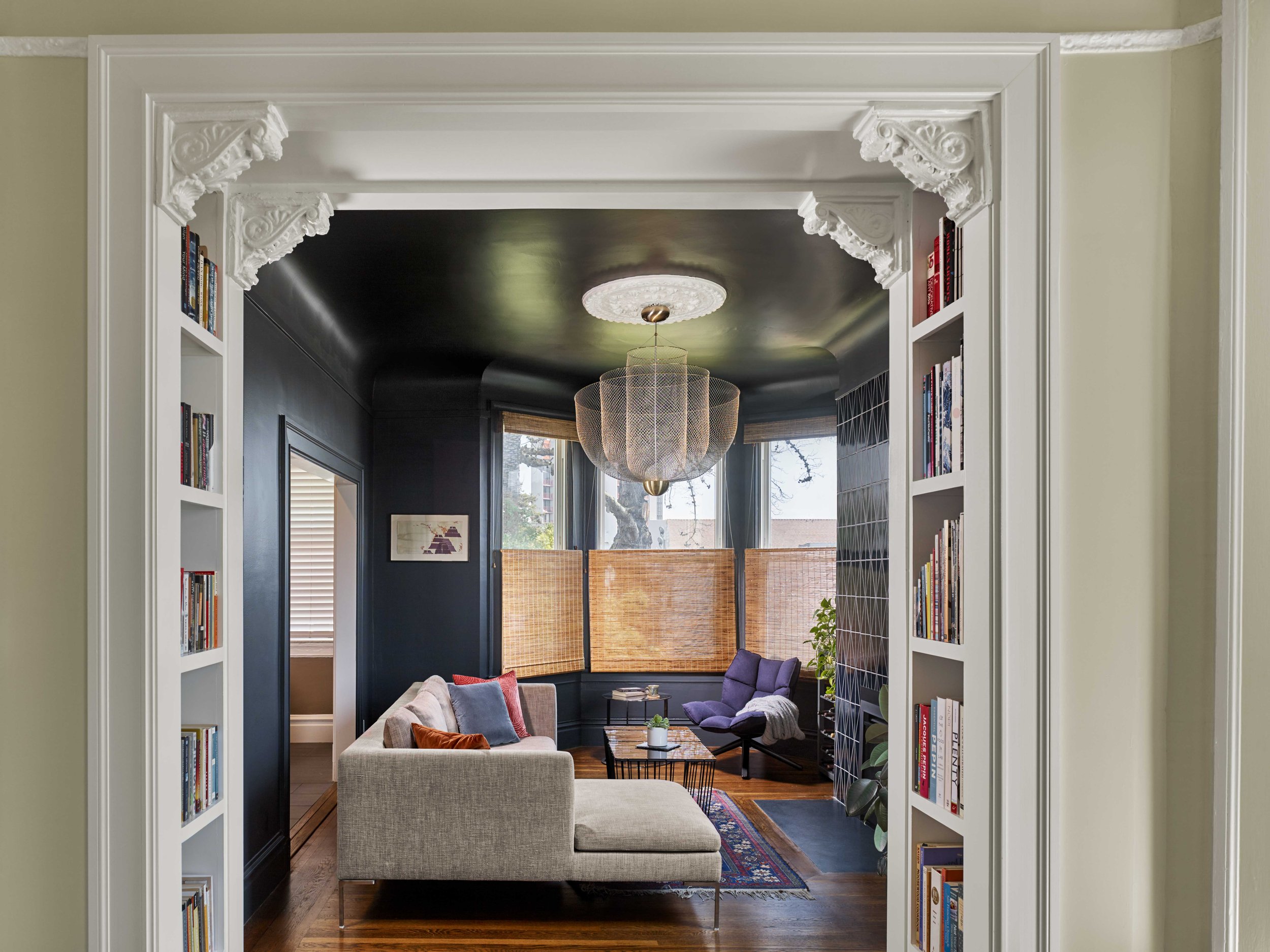 View through an ornate Victorian archway into a navy-walled living room with built-in bookshelves and bay windows