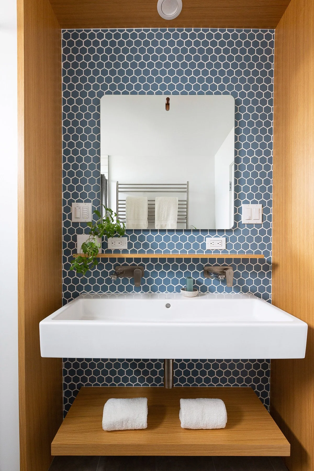 Powder room with a blue penny-tile accent wall, floating white vessel sink, wood-framed mirror, and folded towels