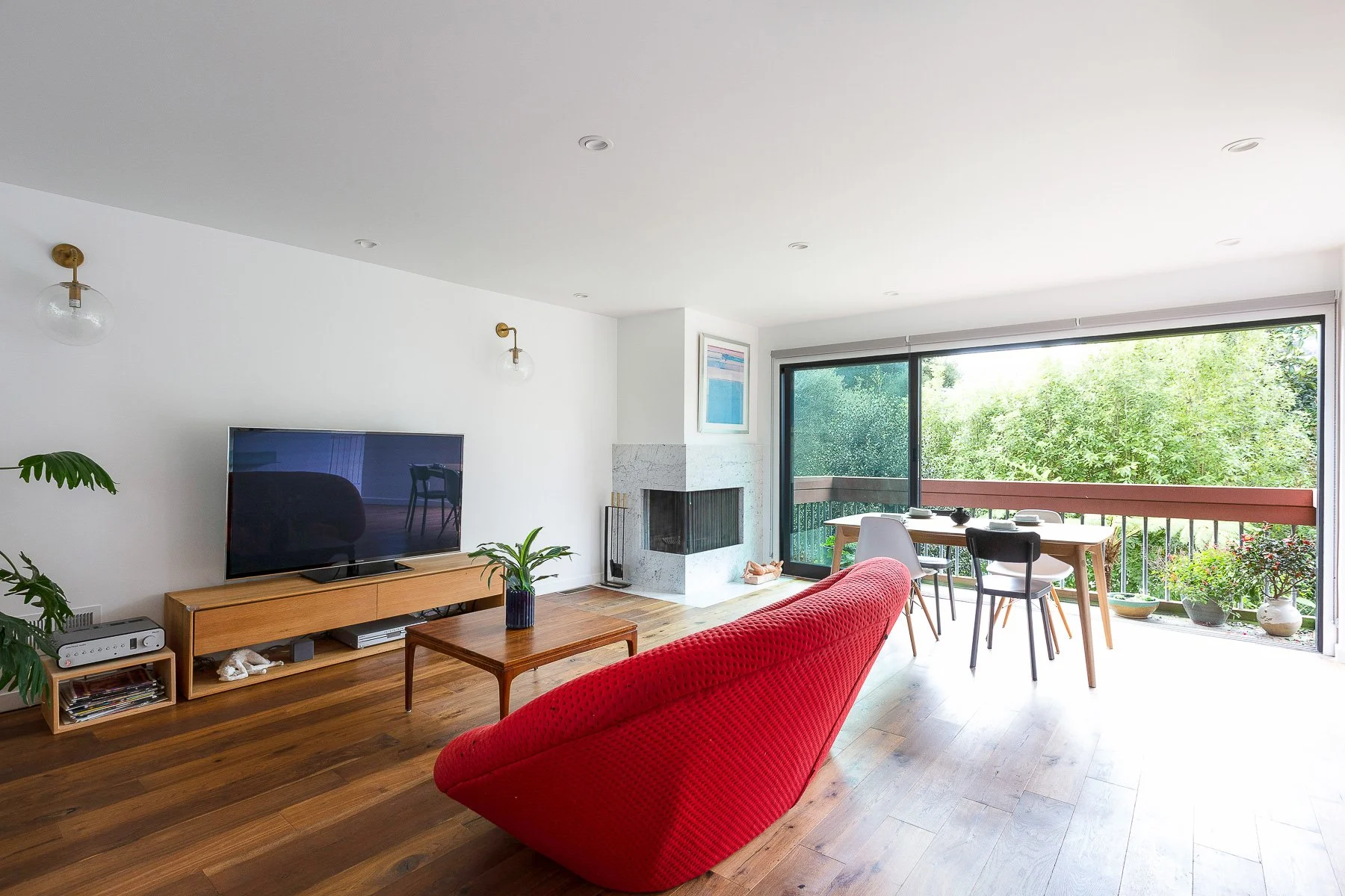 Open living room with a wall-mounted TV, red curved sofa, wood media console, and sliding glass doors to a deck