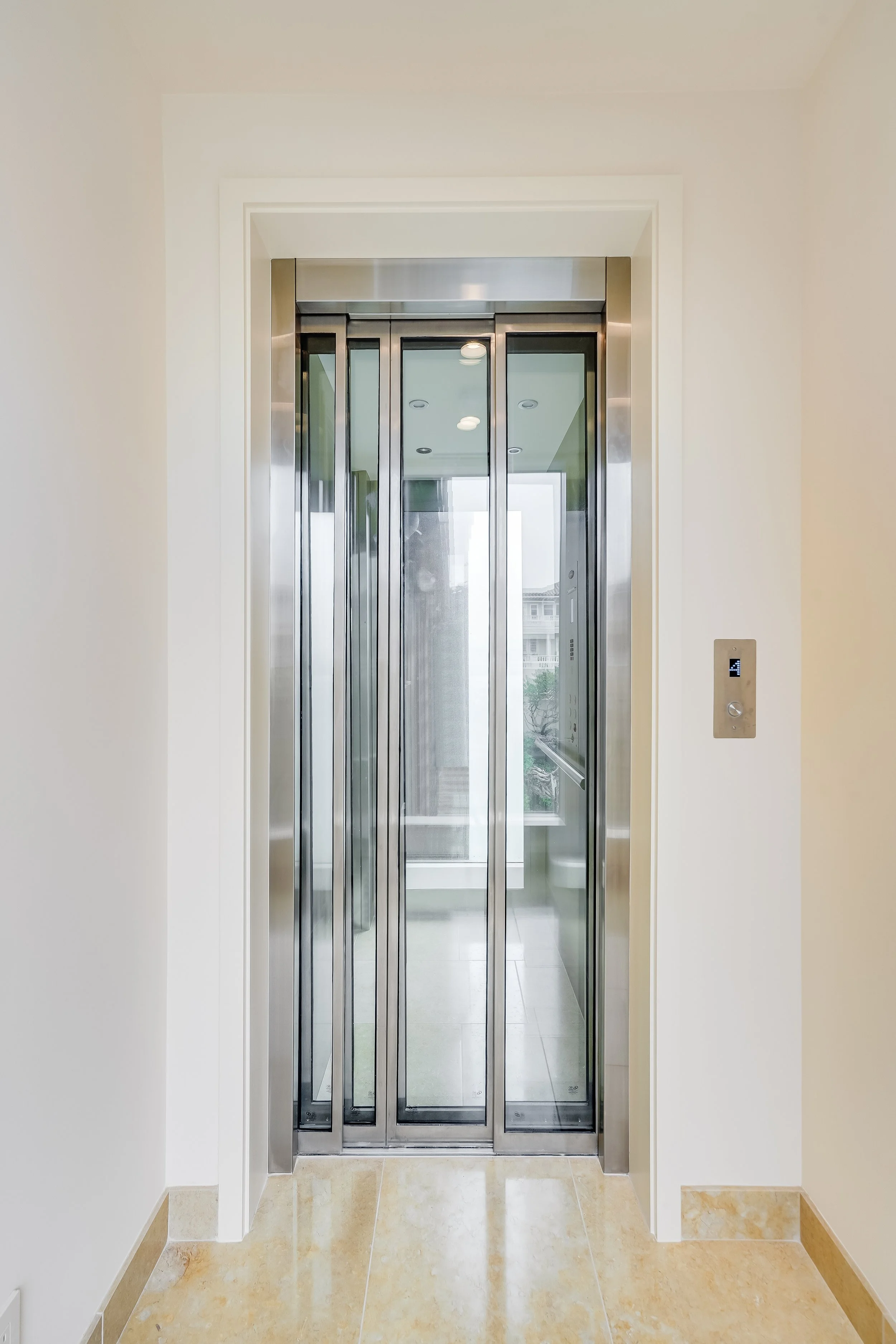 Stainless steel and glass residential elevator with the door open on a wood-floored landing