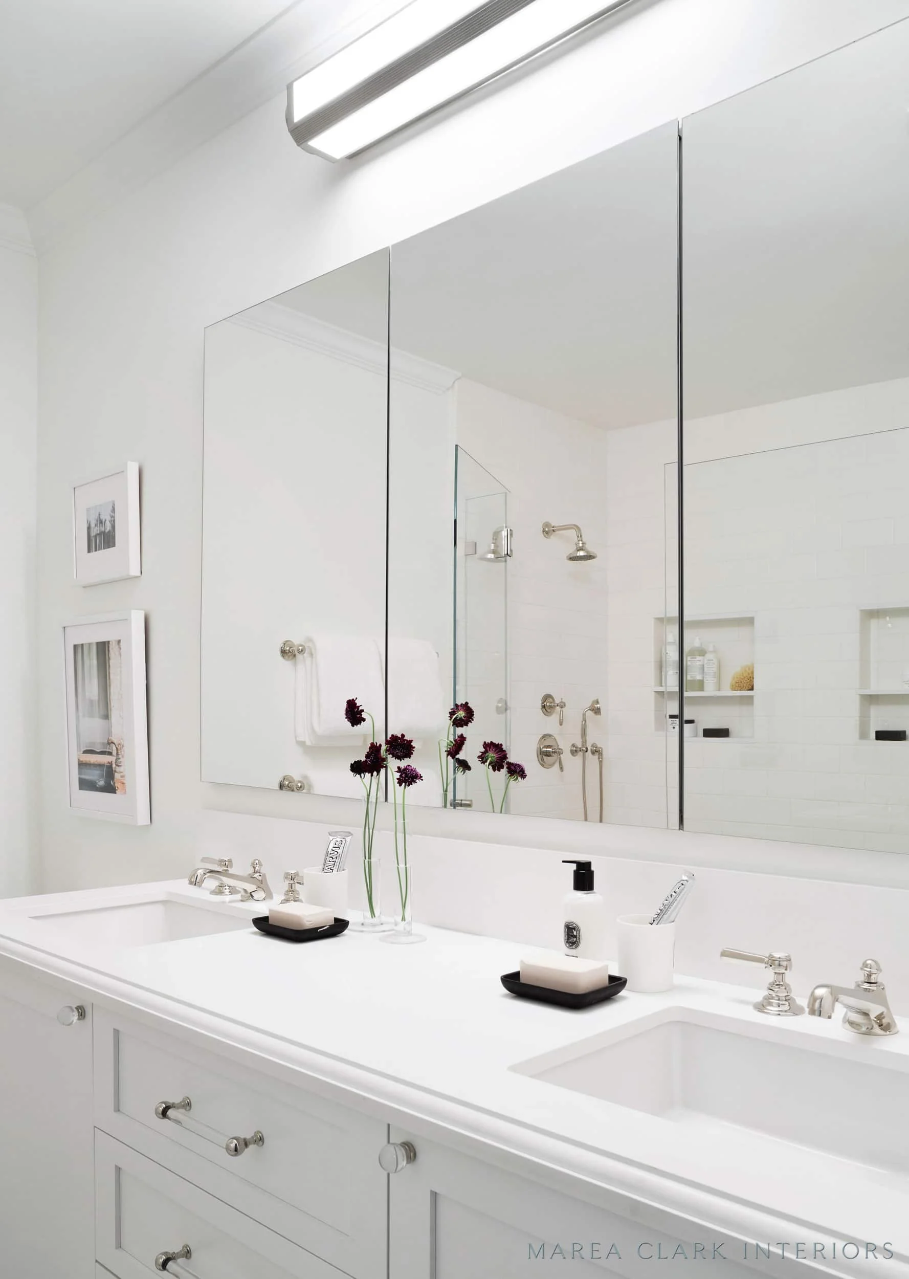 White bathroom with a double vanity, large mirror, wall-mounted light bar, and polished nickel fixtures