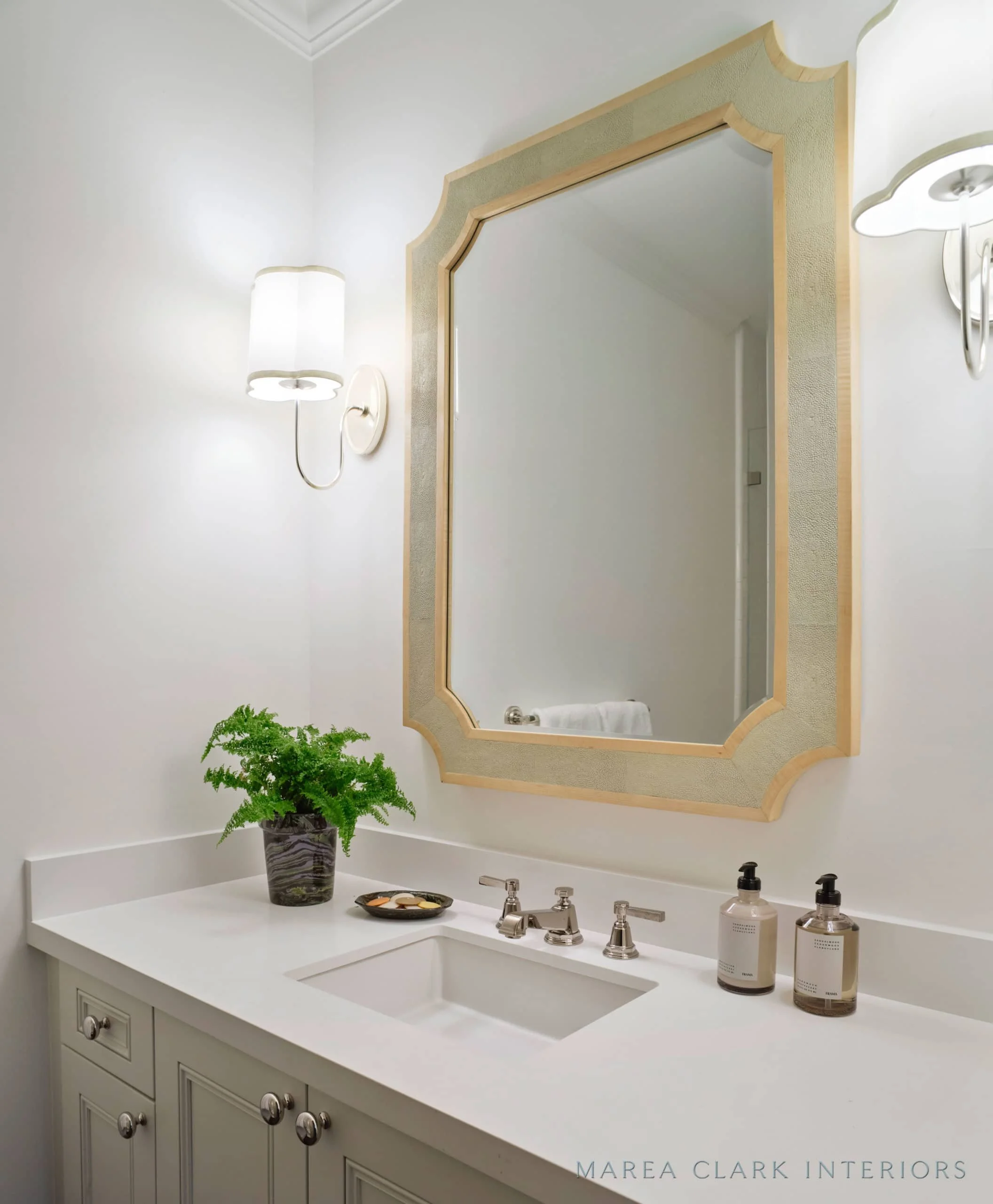 Powder room with a gold-framed mirror, wall sconces, undermount sink, and a potted fern