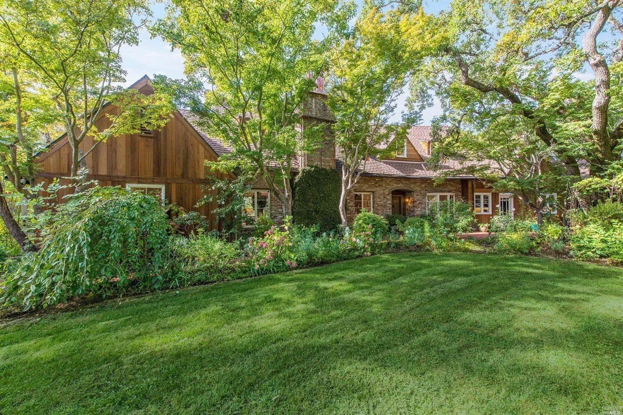 Exterior view of the home with a wood and stone facade set behind a large green lawn and mature trees