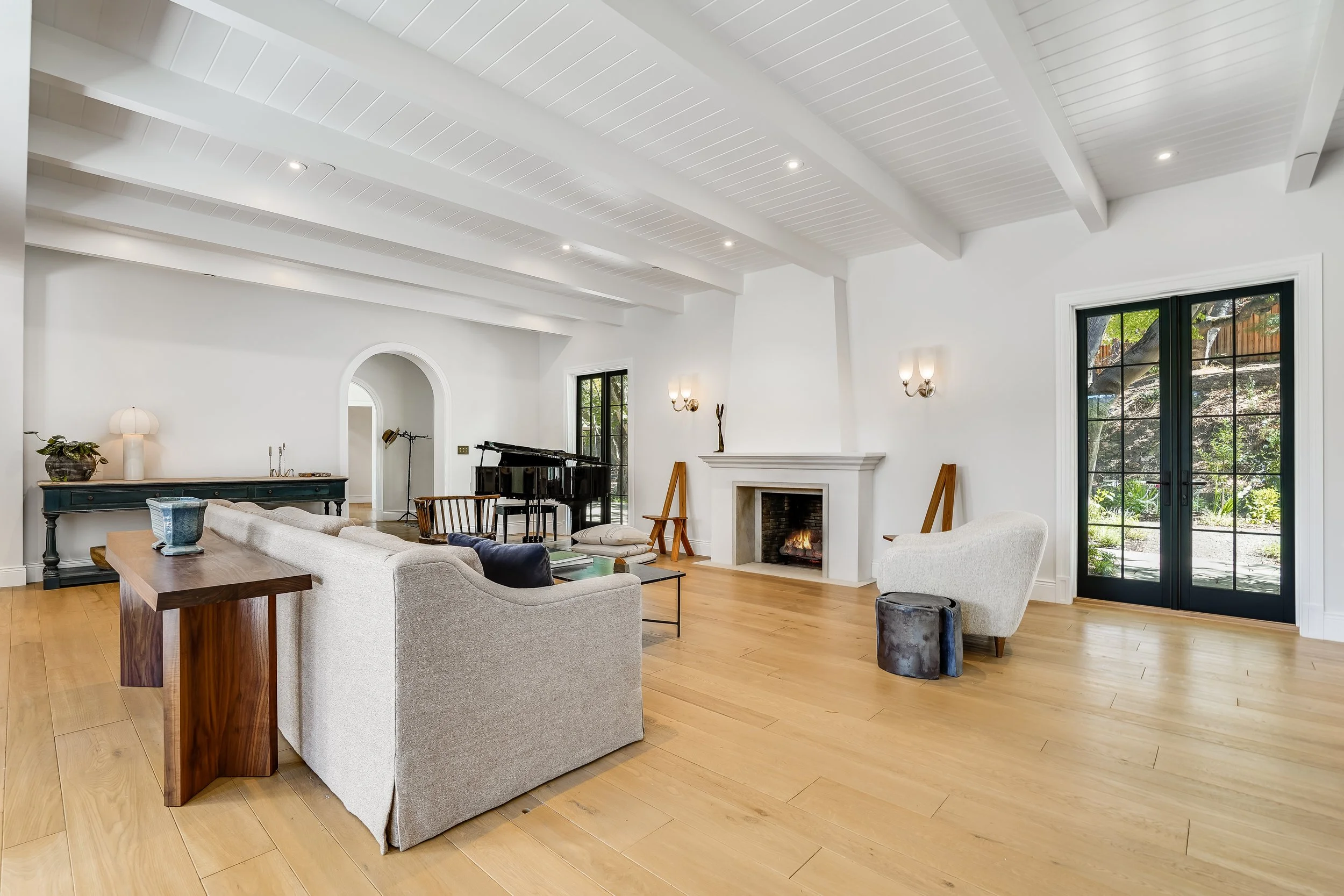 Great room with a white beamed ceiling, fireplace, arched openings, wood island, and glass doors to the garden