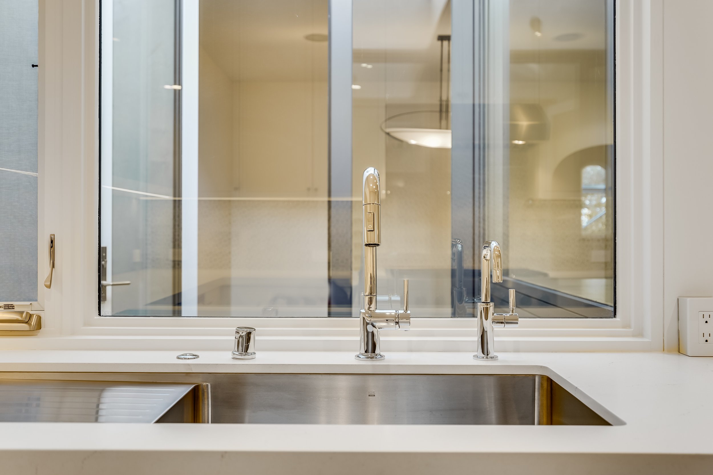 Close-up of a white kitchen counter with an undermount stainless sink and gooseneck faucet beneath a window