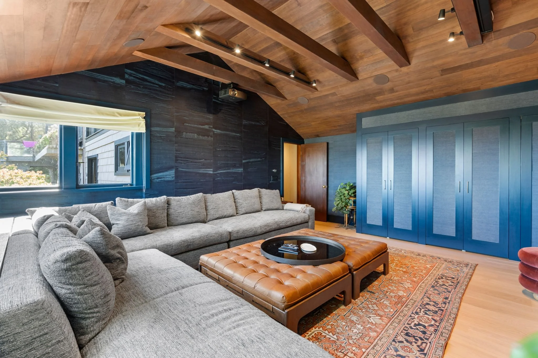 Home theater with vaulted wood ceiling, navy blue built-in cabinetry, gray sectional and leather ottomans