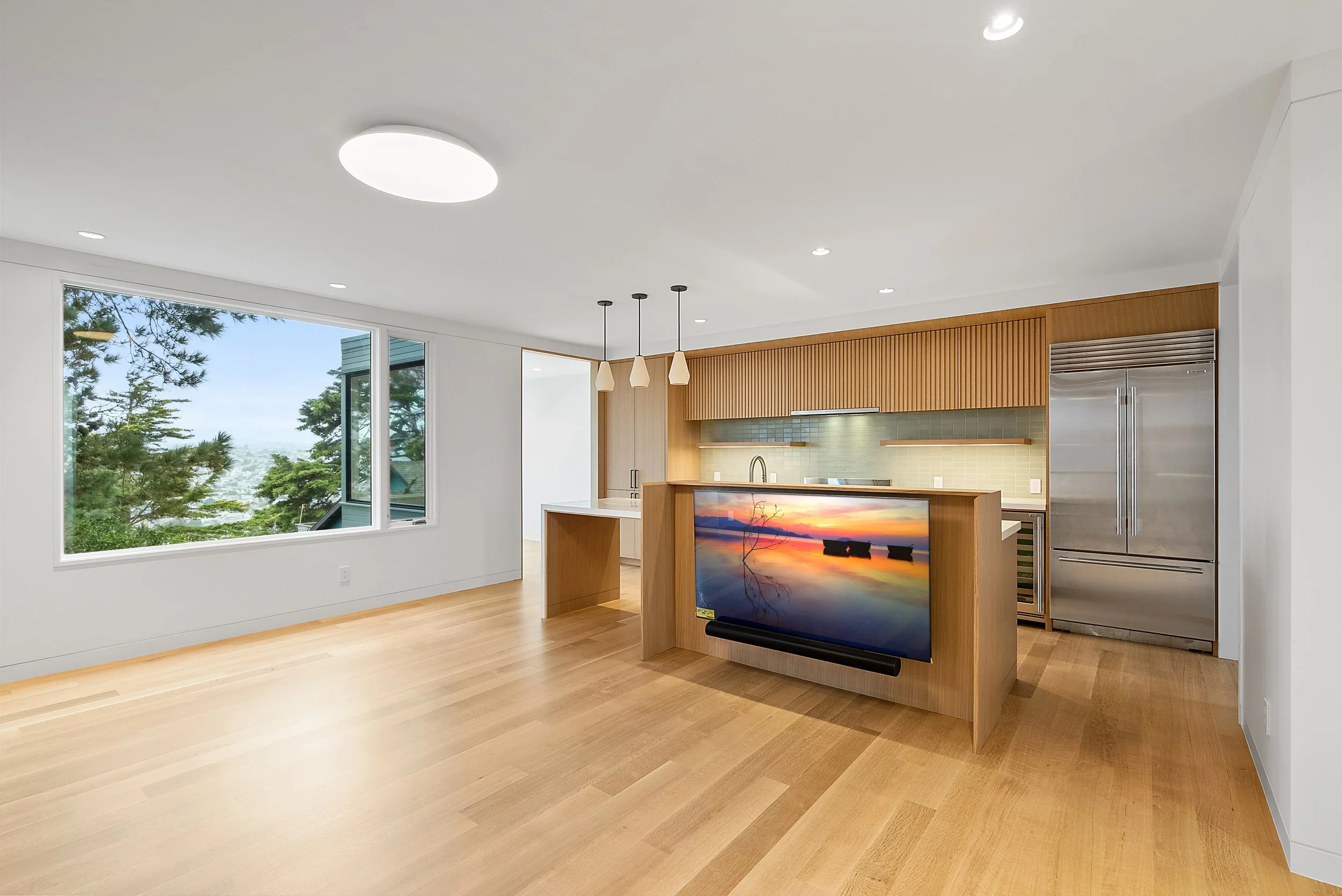 Open-plan living and kitchen with light wood cabinetry, a waterfall island, large windows, and hardwood floors