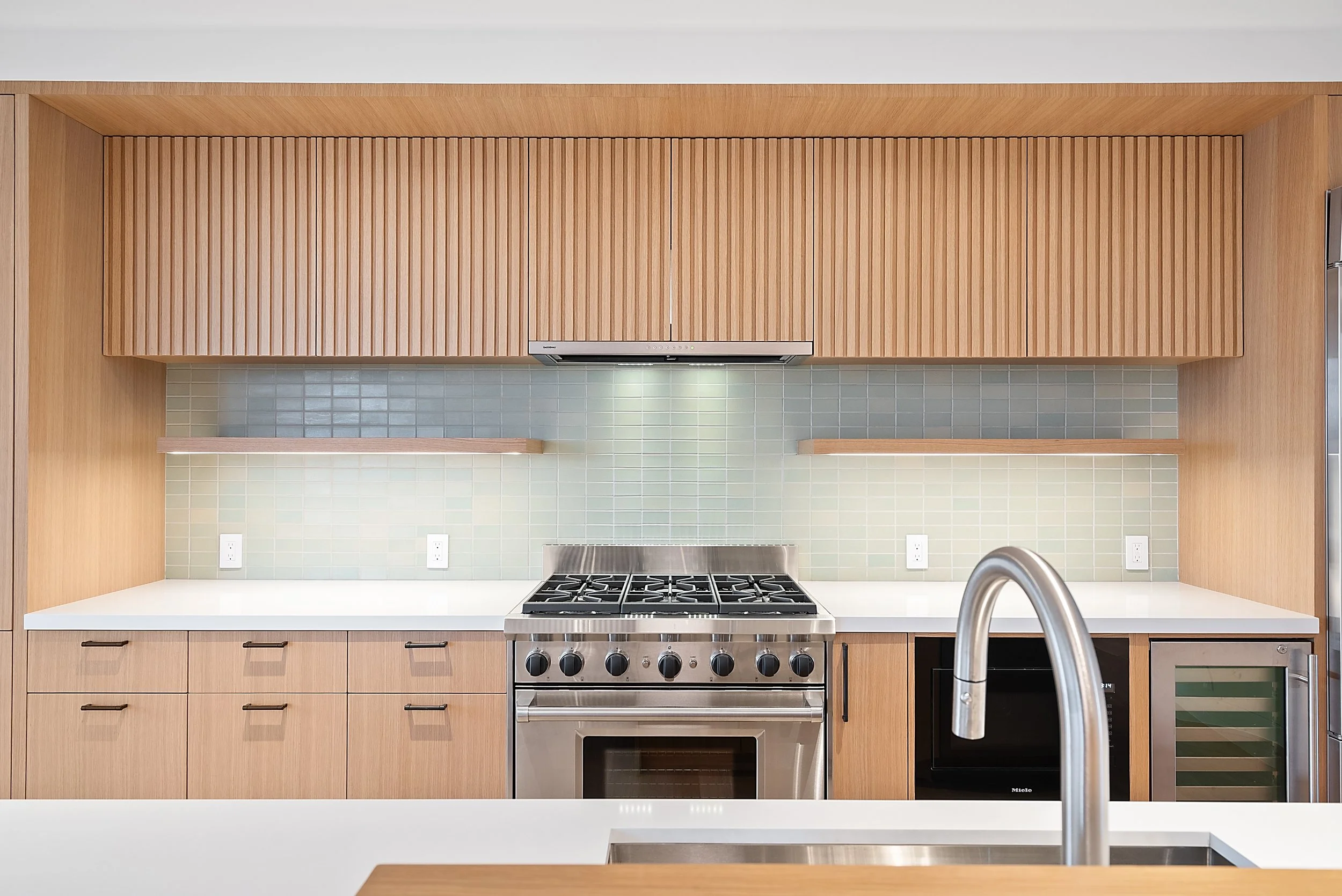 Kitchen with light wood cabinets, a slatted range hood, gas range, wine fridge, and white countertops