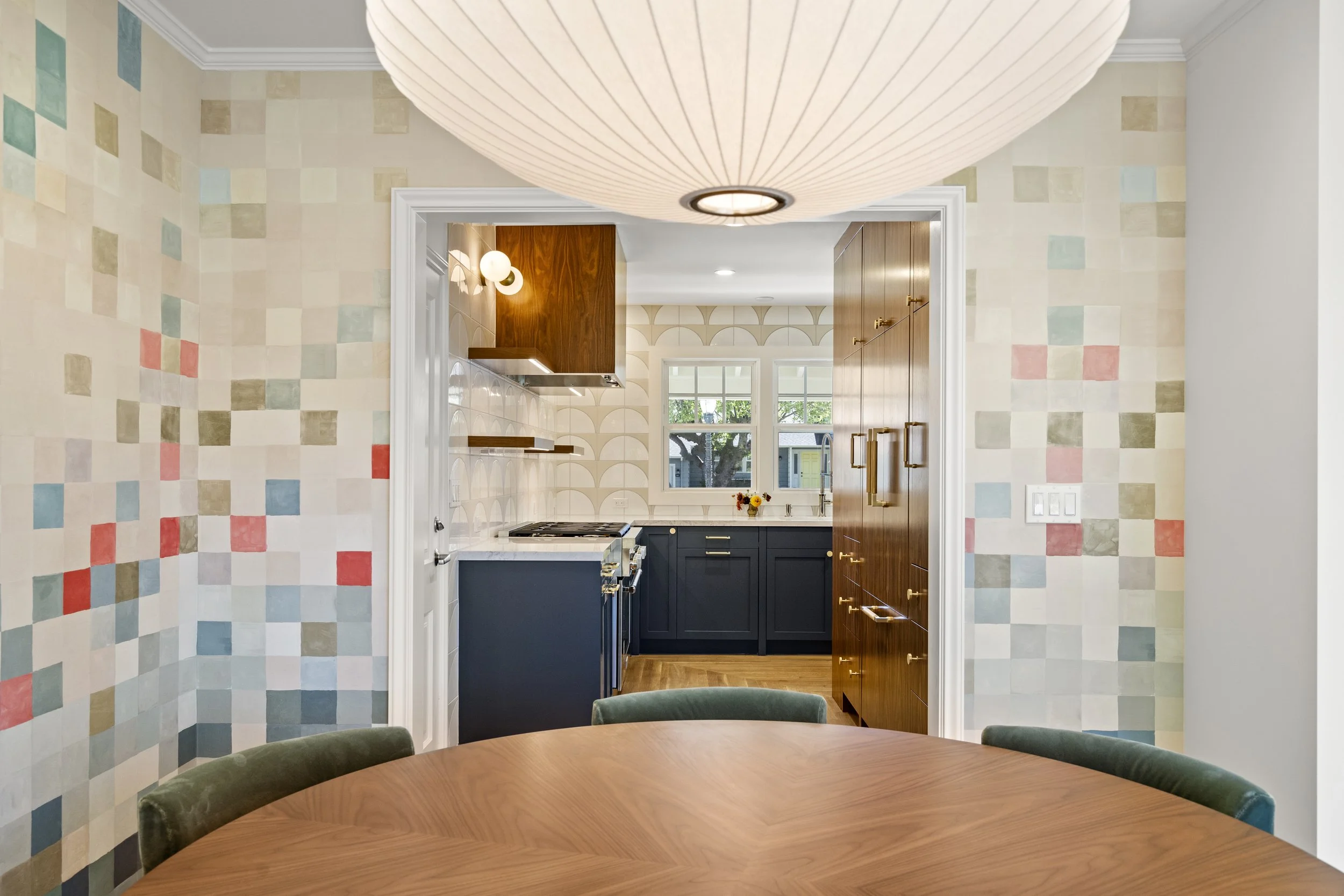 Dining room with a colorful multicolor tile accent wall and a view into a navy kitchen