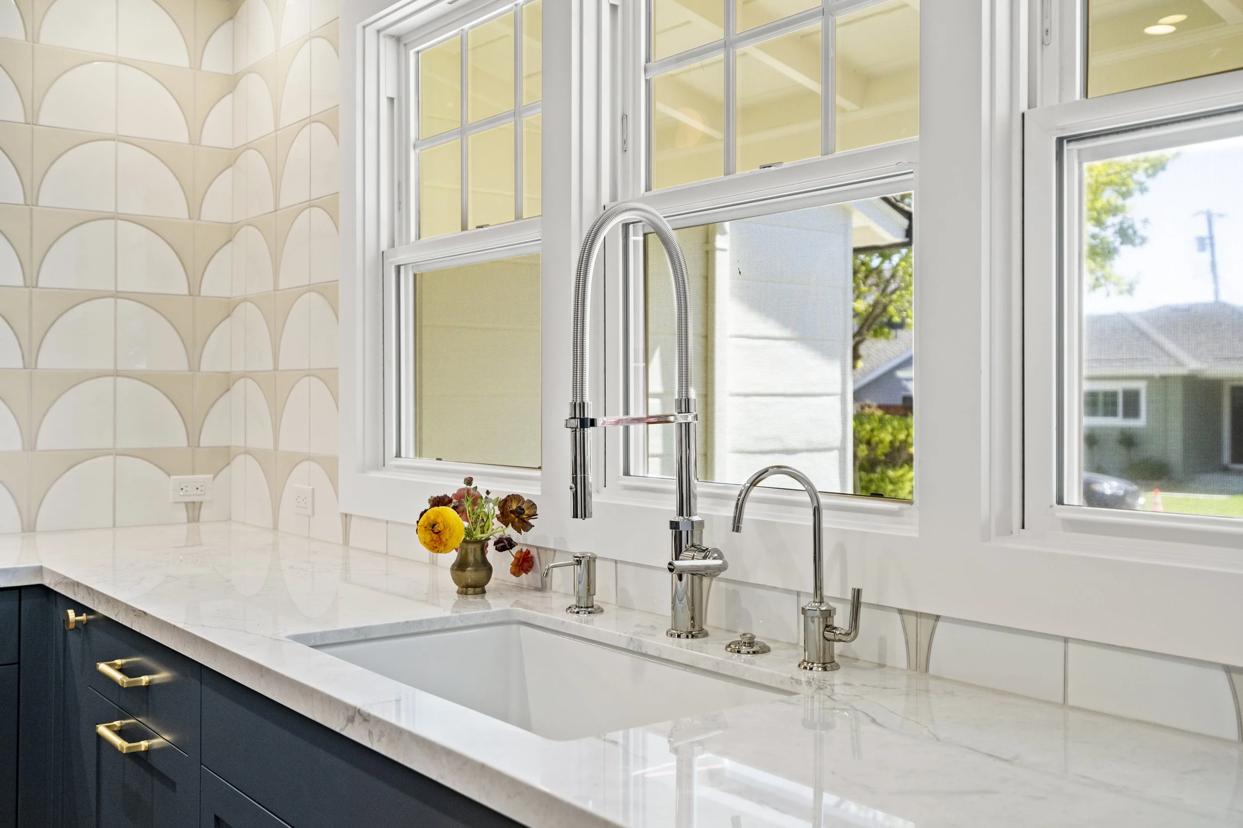 Kitchen sink area with a white undermount sink, gooseneck faucet, scalloped tile, and windows over the counter
