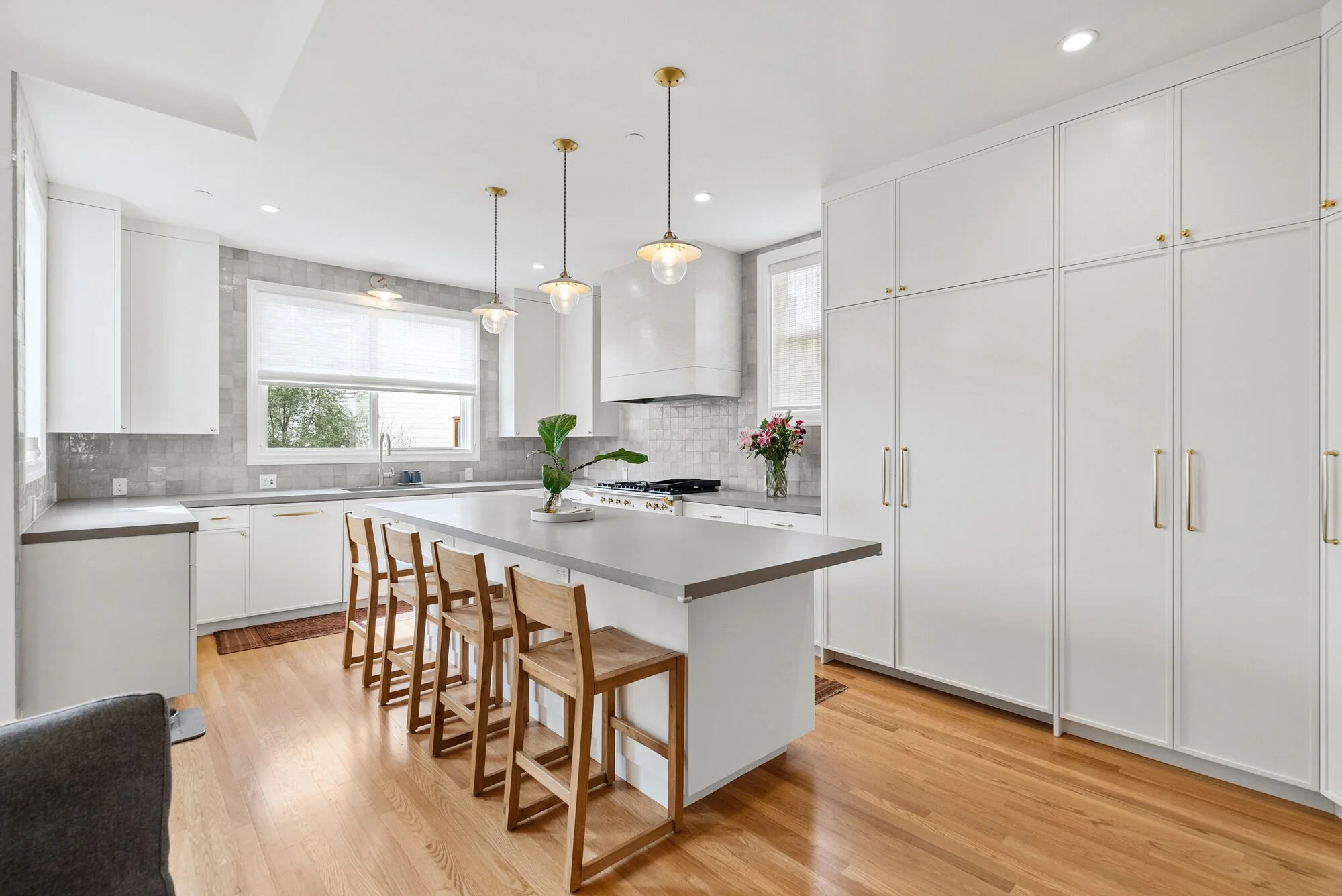 White kitchen with an island, wood bar stools, pendant lights, a subway tile backsplash, and hardwood floors
