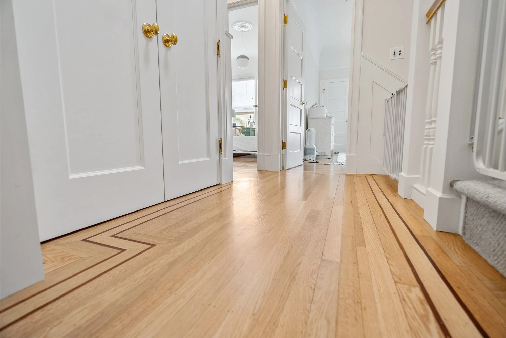 Entry hallway with white paneled doors, ornate molding, and an inlaid hardwood floor