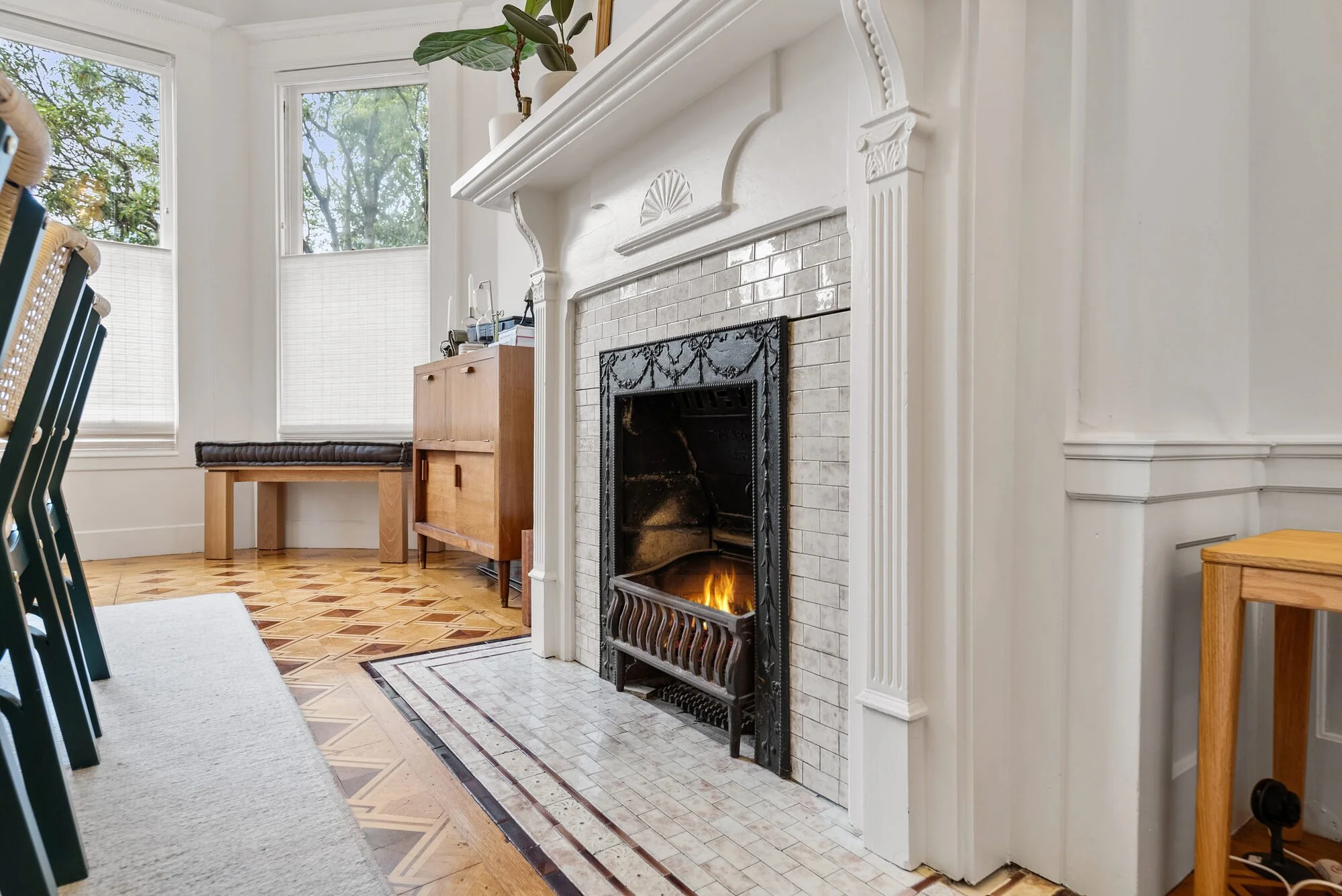Living room with a white mantel fireplace, a decorative tile surround, a bay window, and hardwood floors