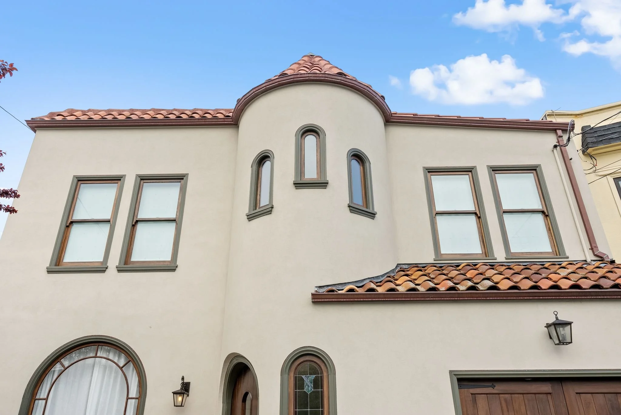 Two-story stucco Spanish-style home with a red tile roof, turret, and arched windows against a blue sky