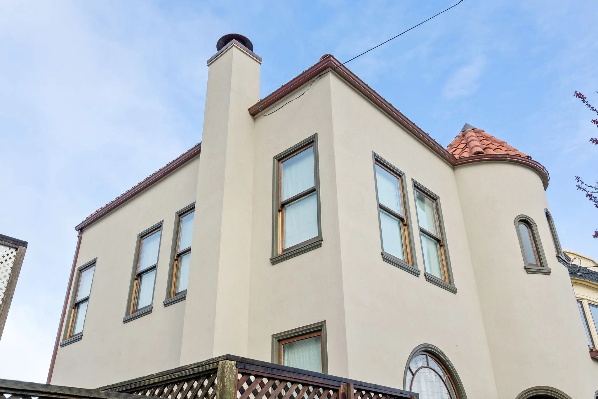 Rear exterior of a stucco home with a tile roof, multiple windows, and a wood pergola