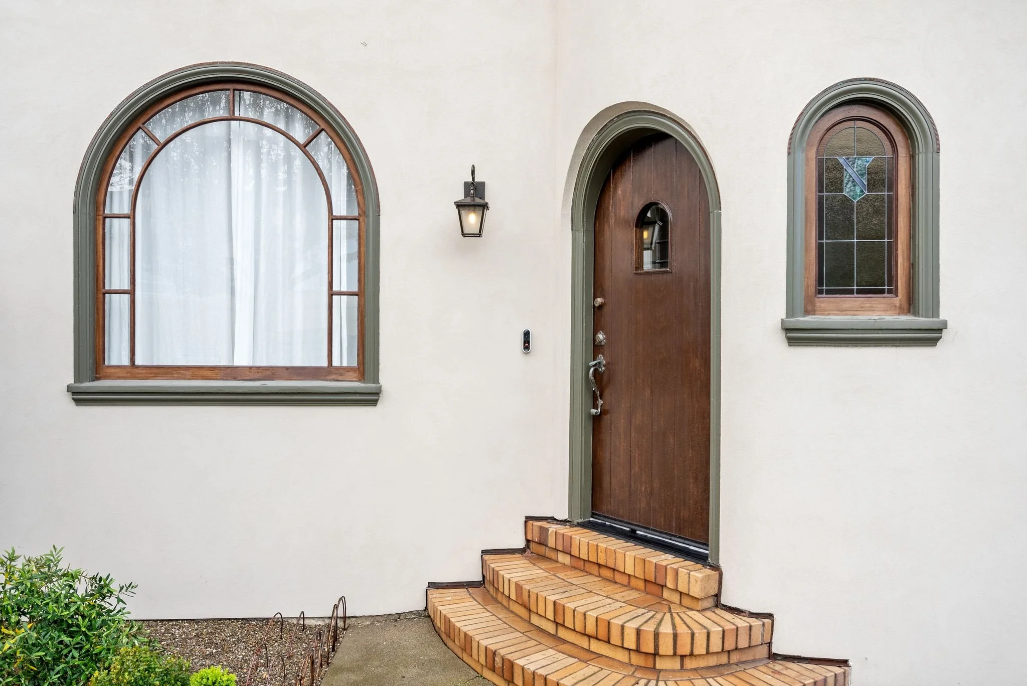 Home entrance with a wood arched front door, brick steps, and a large arched window