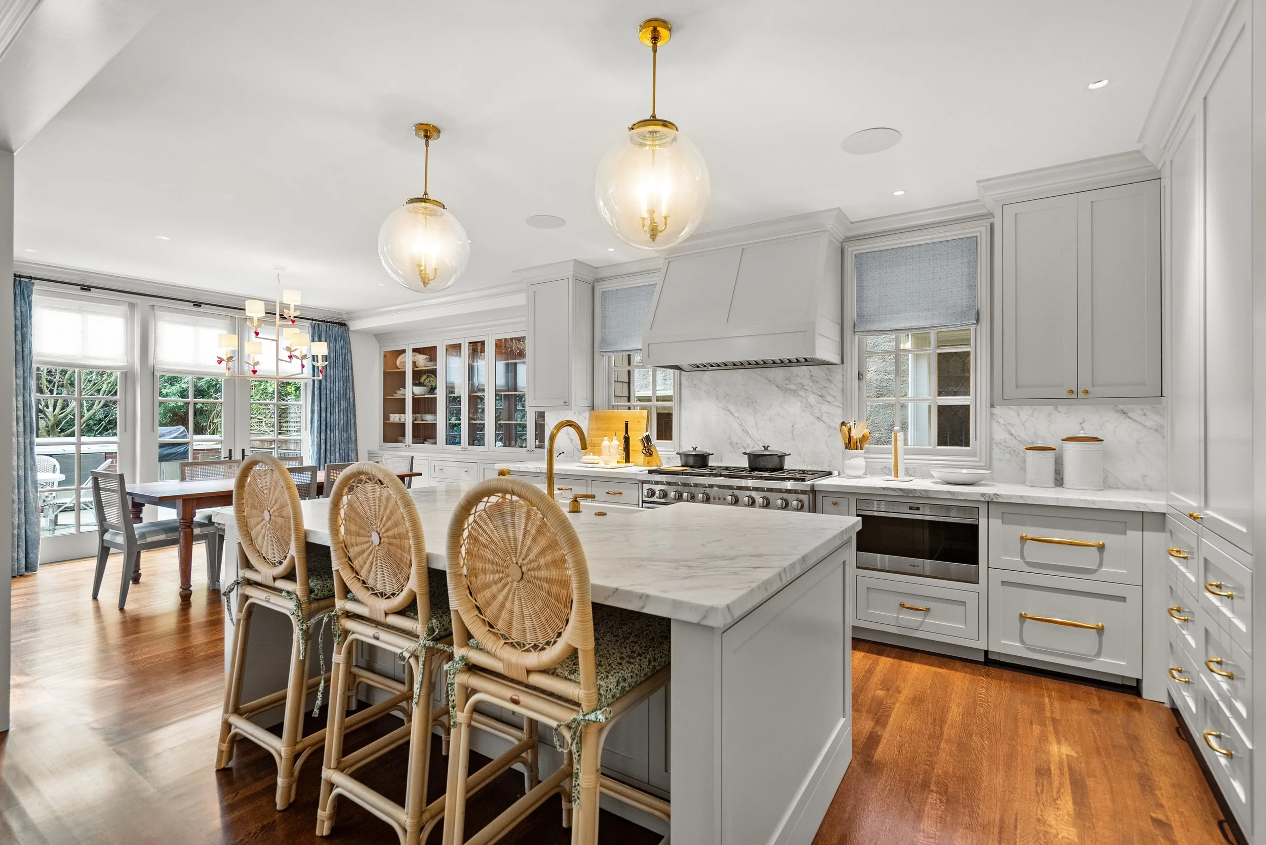 Kitchen with white cabinets, a marble island, cane-back barstools, glass pendant lights, and hardwood floors