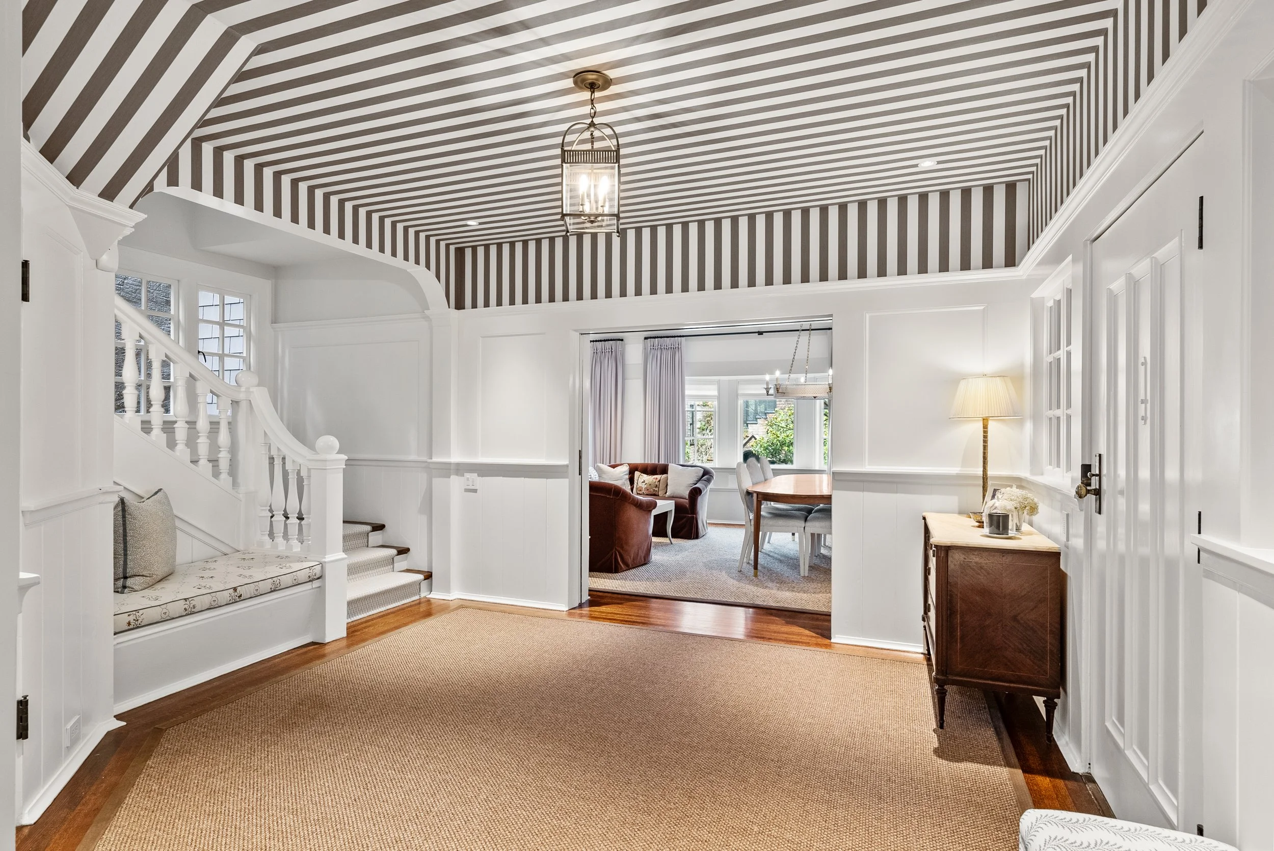 Sitting area with a striped ceiling, white paneling, a window-seat bench, and a sisal runner