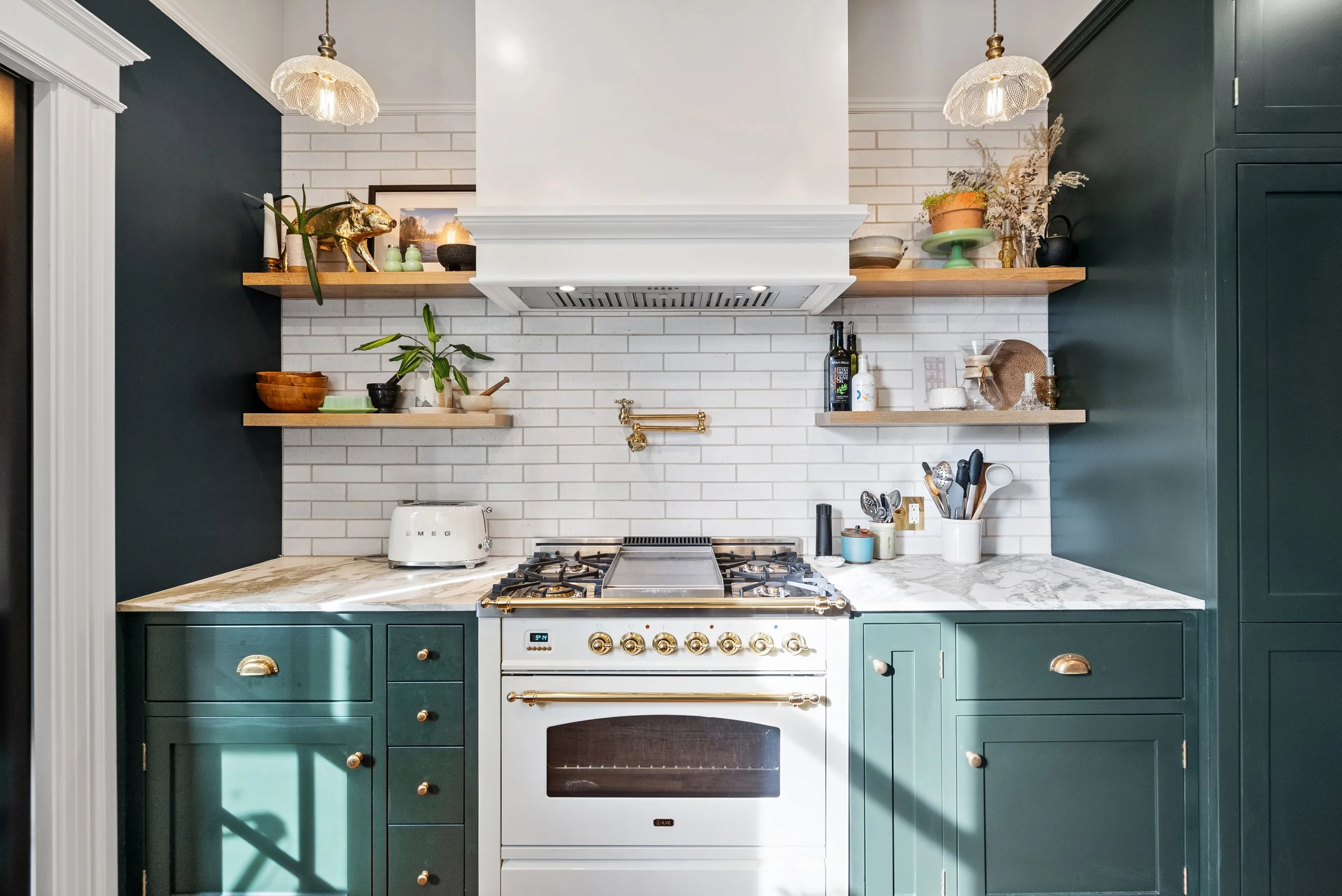 Dark green kitchen with a white range and hood, a subway tile backsplash, open wood shelves, and brass hardware