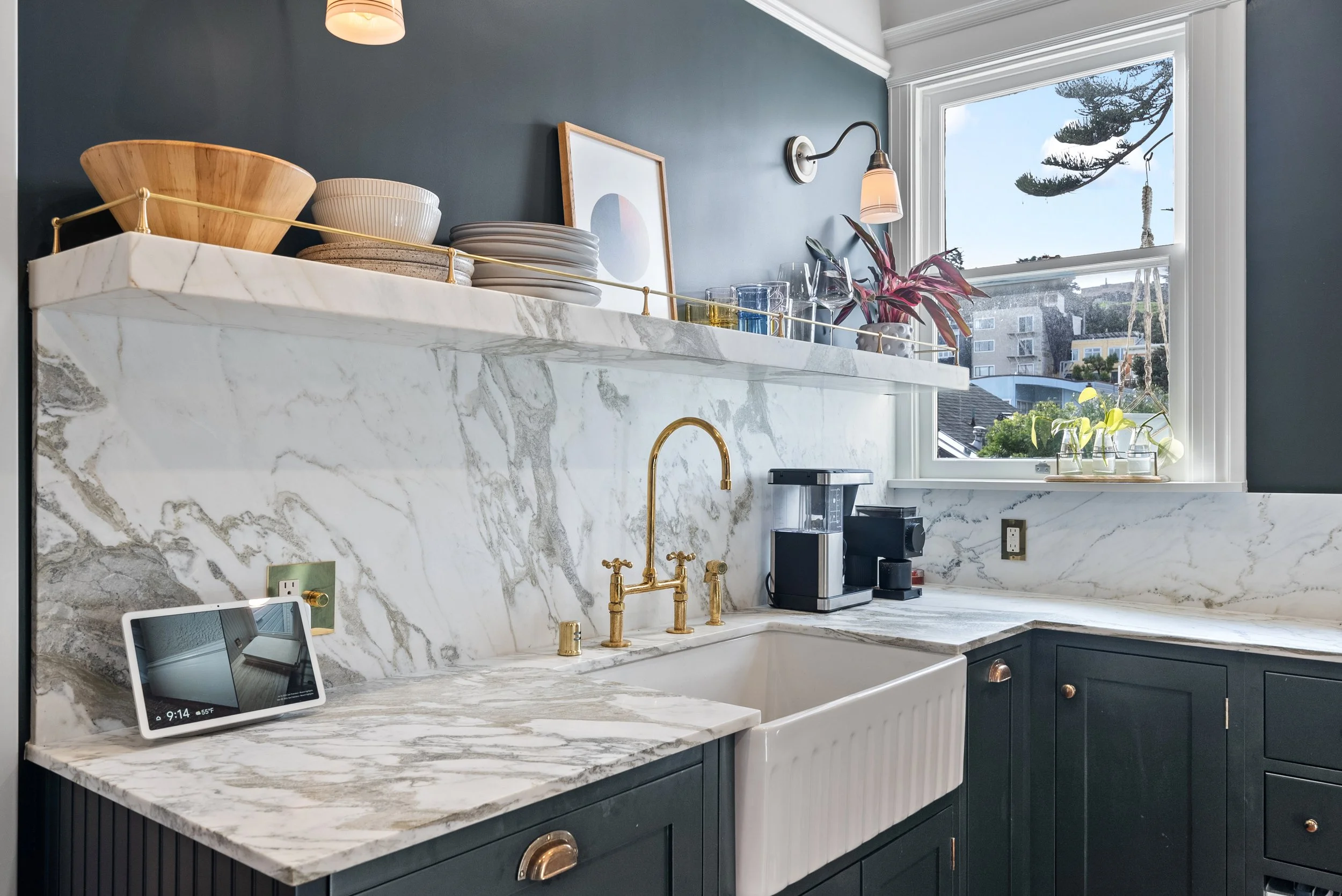 Kitchen corner with a marble farmhouse sink, a brass faucet, a marble backsplash, and a window with a city view