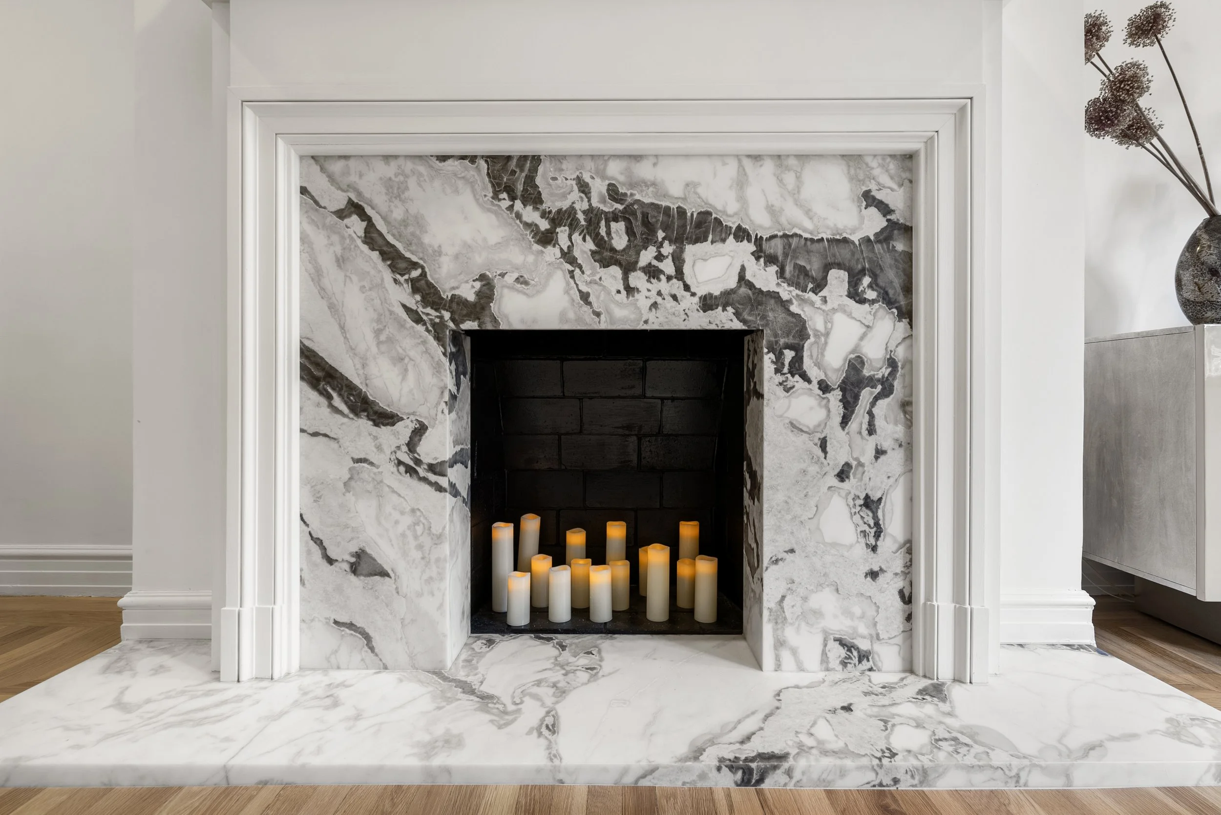 White marble fireplace surround with lit pillar candles in the firebox