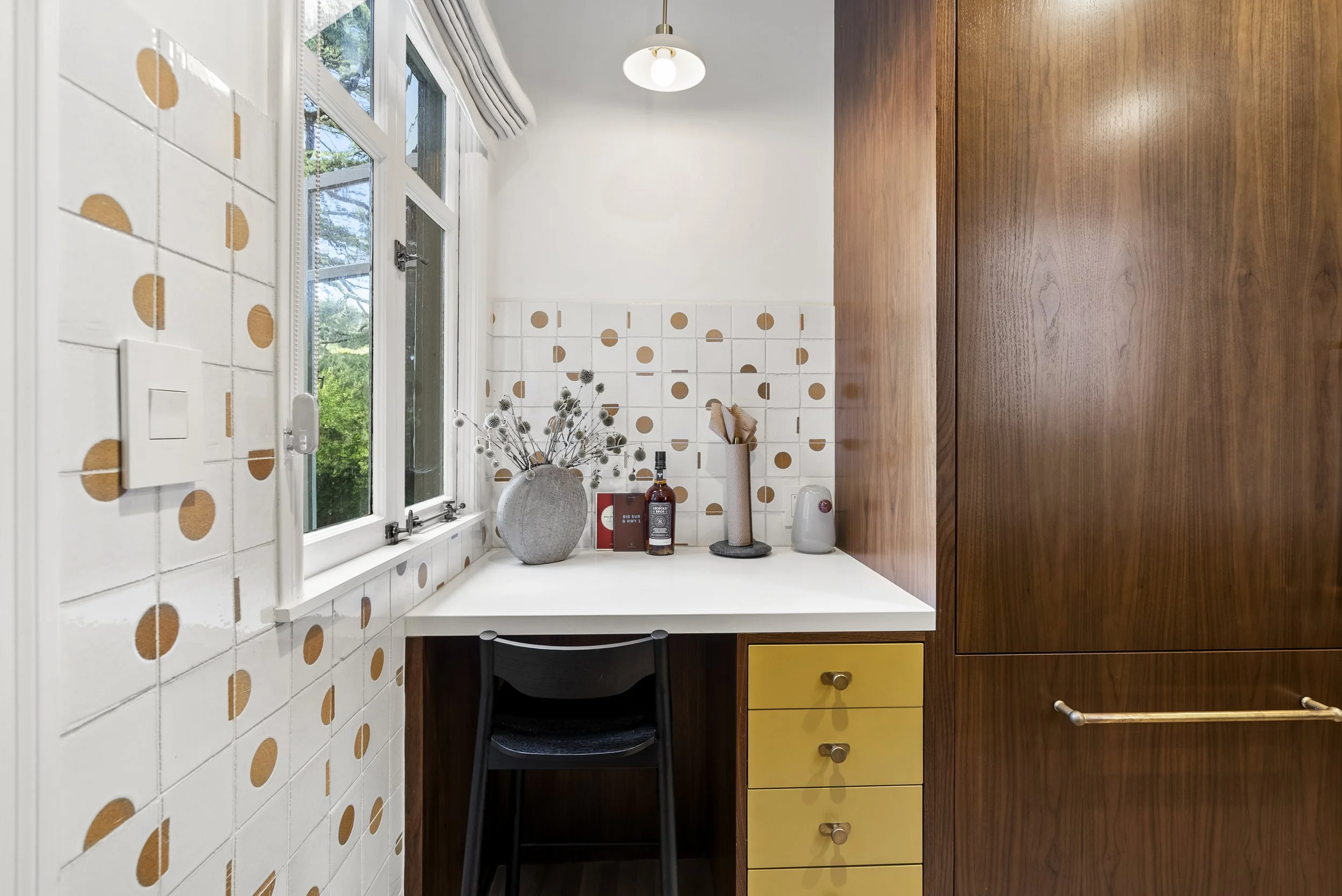 Home office nook with a white desk, walnut cabinetry, and a gold-and-white polka-dot tile wall