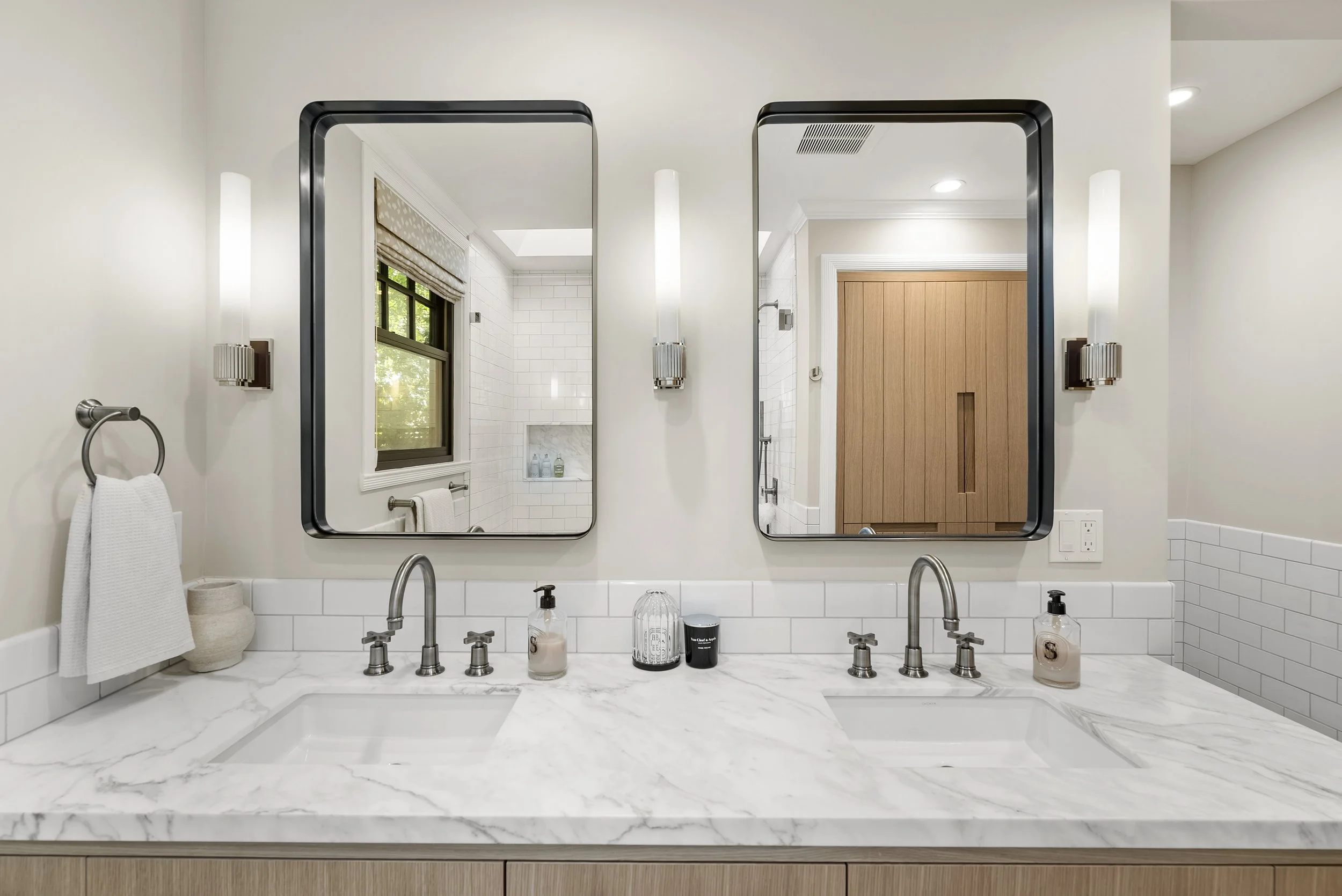 Double vanity with a marble countertop, twin black-framed mirrors, wall sconces, and polished nickel faucets