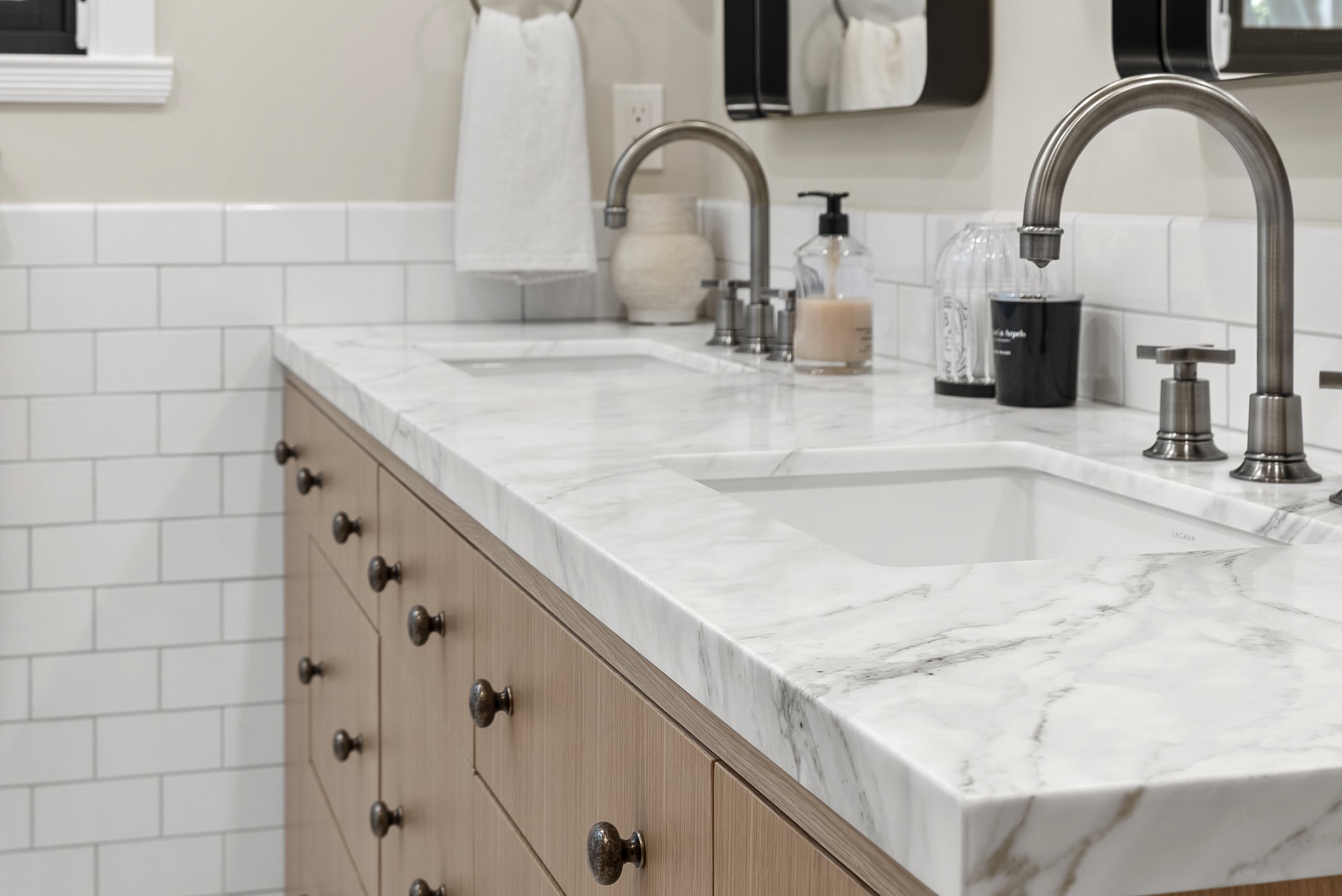 Close-up of a wood vanity with a marble countertop, subway tile backsplash, and brushed nickel faucets