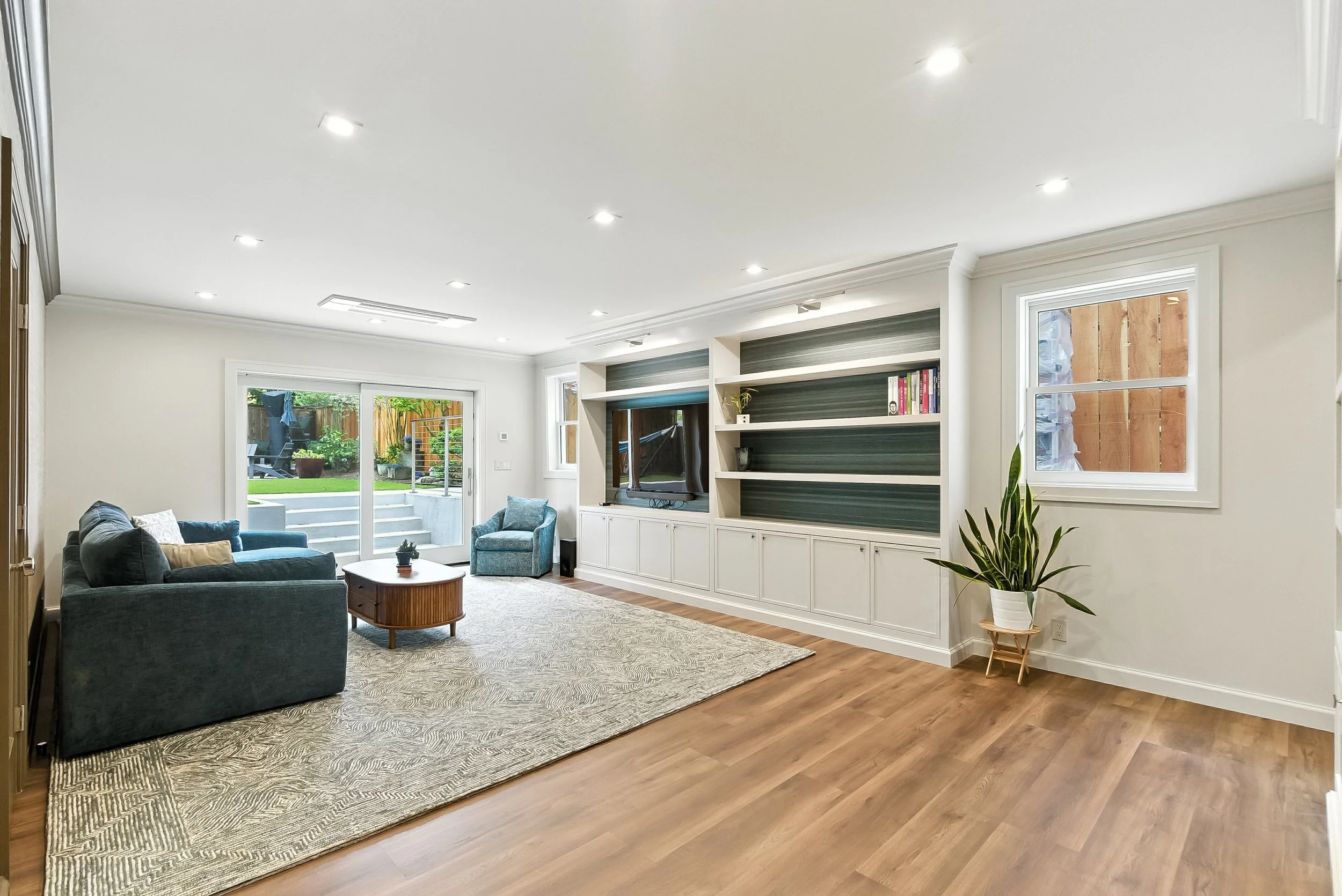 Living room with a built-in media wall, blue sofas, an area rug, hardwood floors, and glass doors to the yard