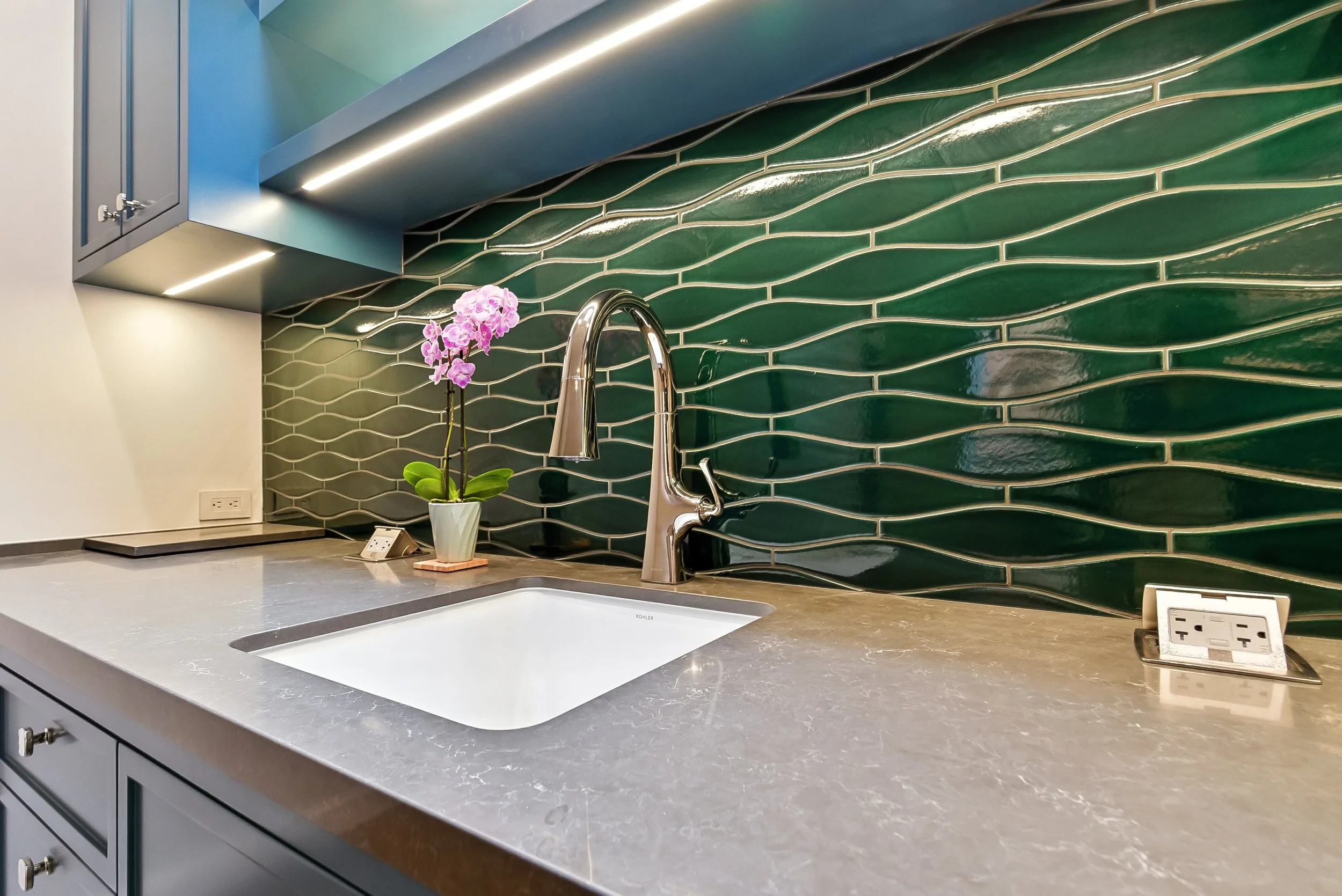 Wet bar with a green tile backsplash, a stone countertop, an undermount sink, and a brass faucet