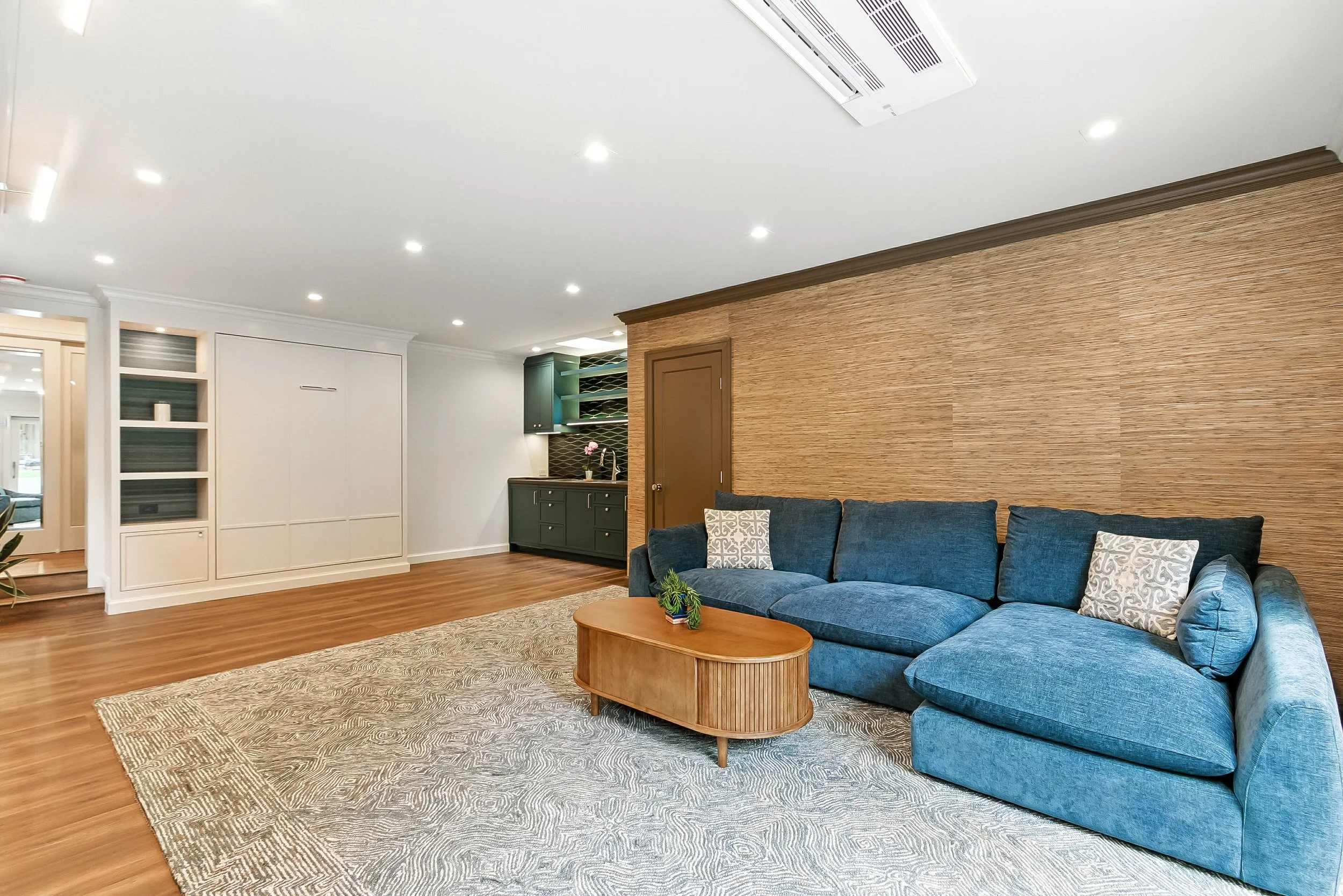 Living room with a blue sectional sofa, a wood accent wall, a round coffee table, and an area rug