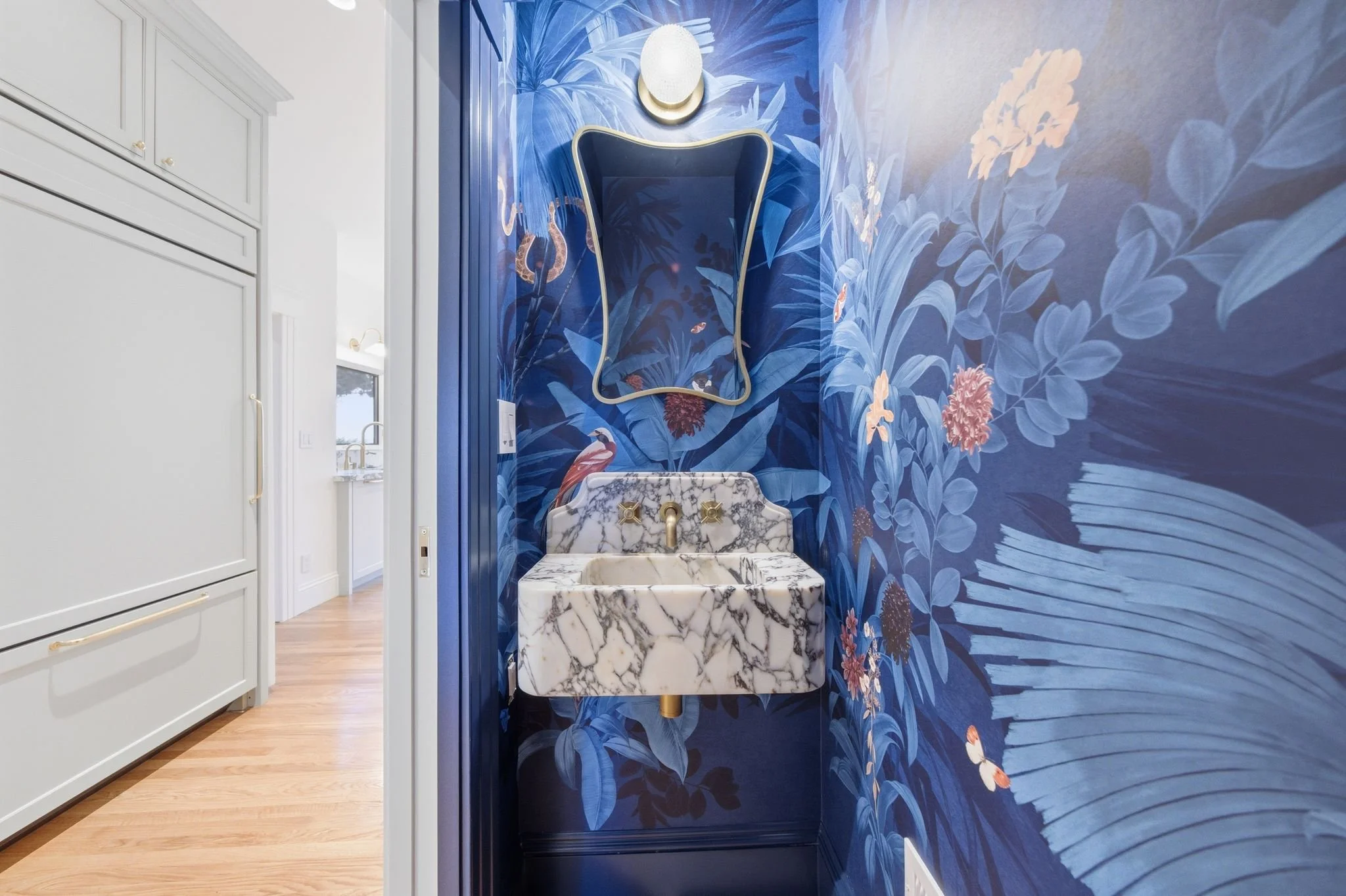 Powder room with dramatic blue botanical wallpaper, a marble wall-mounted sink, and a curvy black-framed mirror