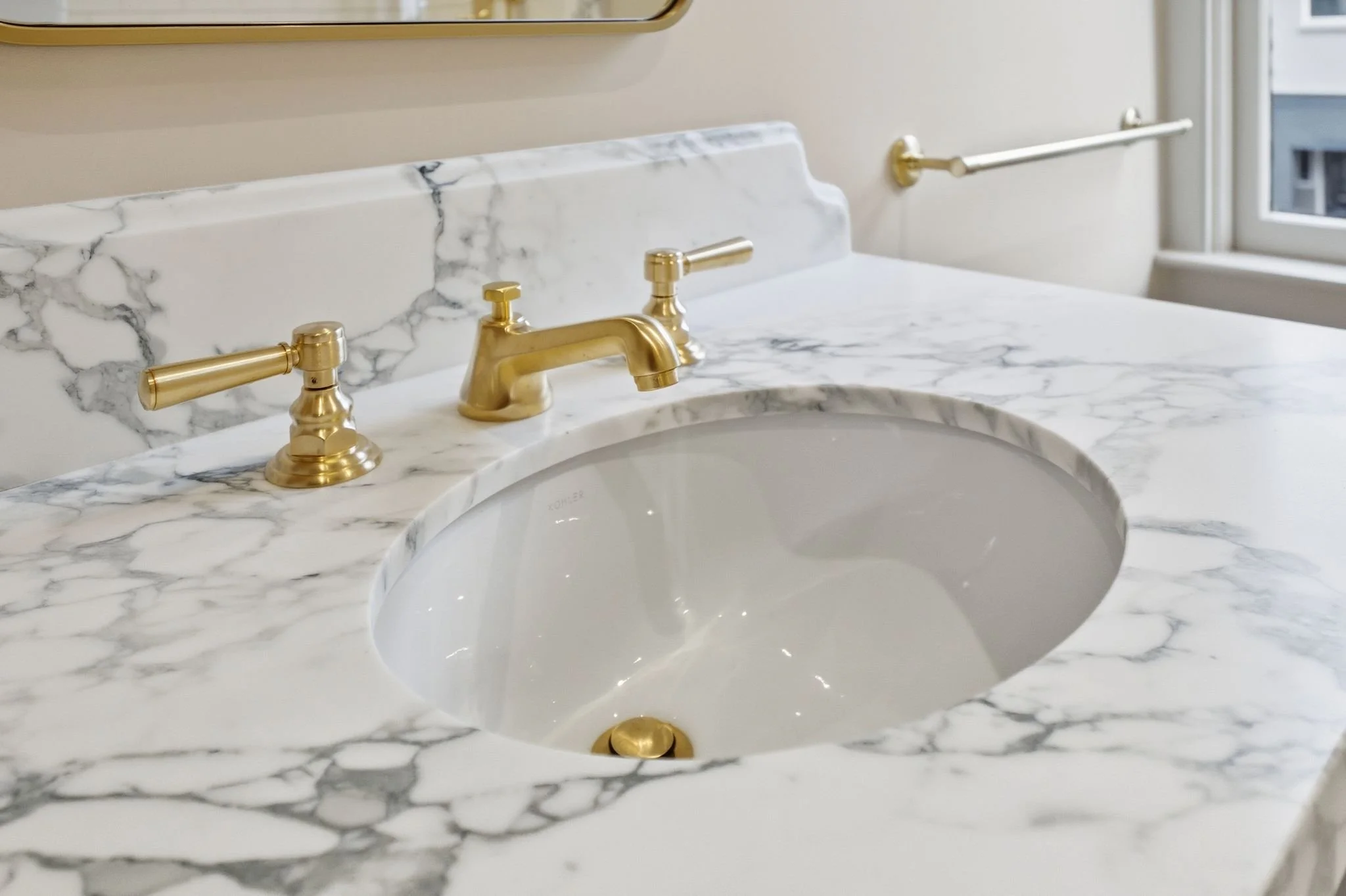 Close-up of a marble vanity countertop with an undermount sink and a gold widespread faucet