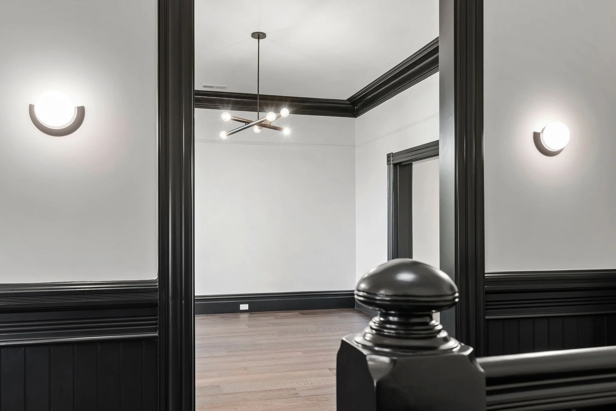 Living room with black-painted Victorian trim, half-moon sconces, brass chandelier and turned newel post