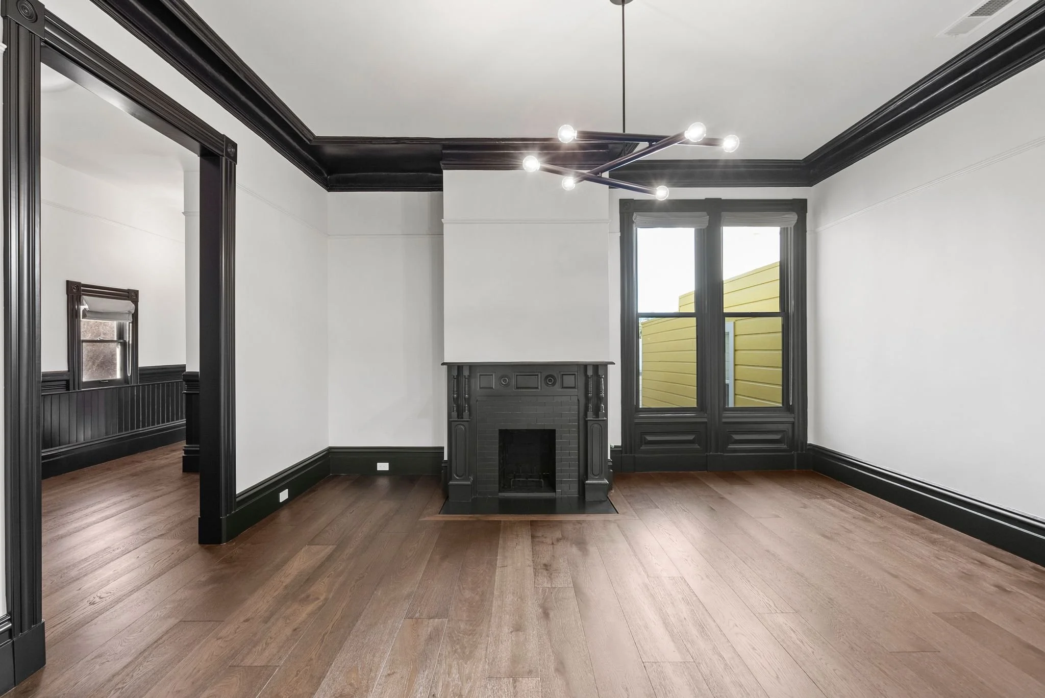 Double parlor with restored black fireplace mantel, black crown molding and wide-plank oak floors